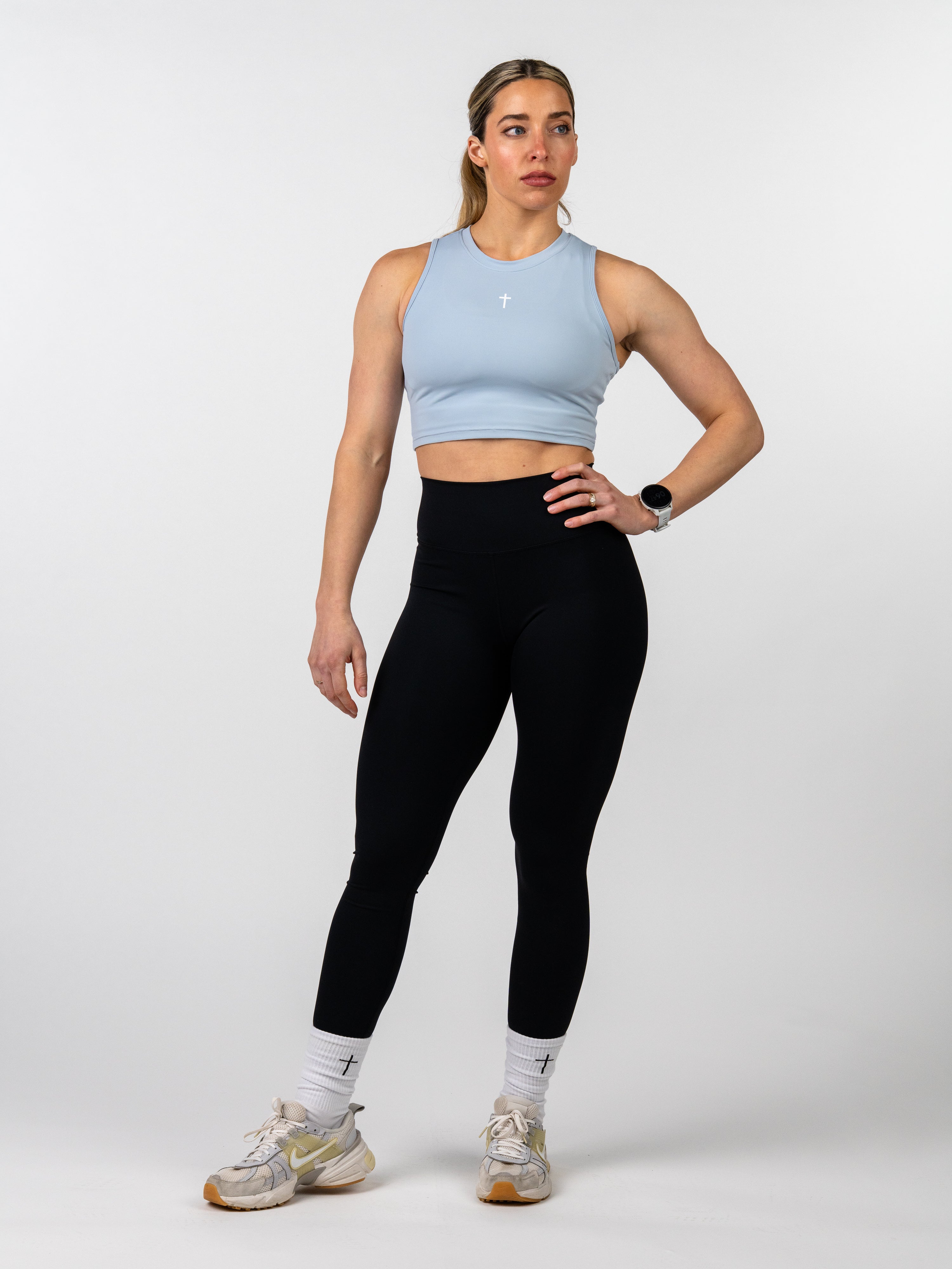 Woman wearing a light blue sports bra and black leggings on a white background
