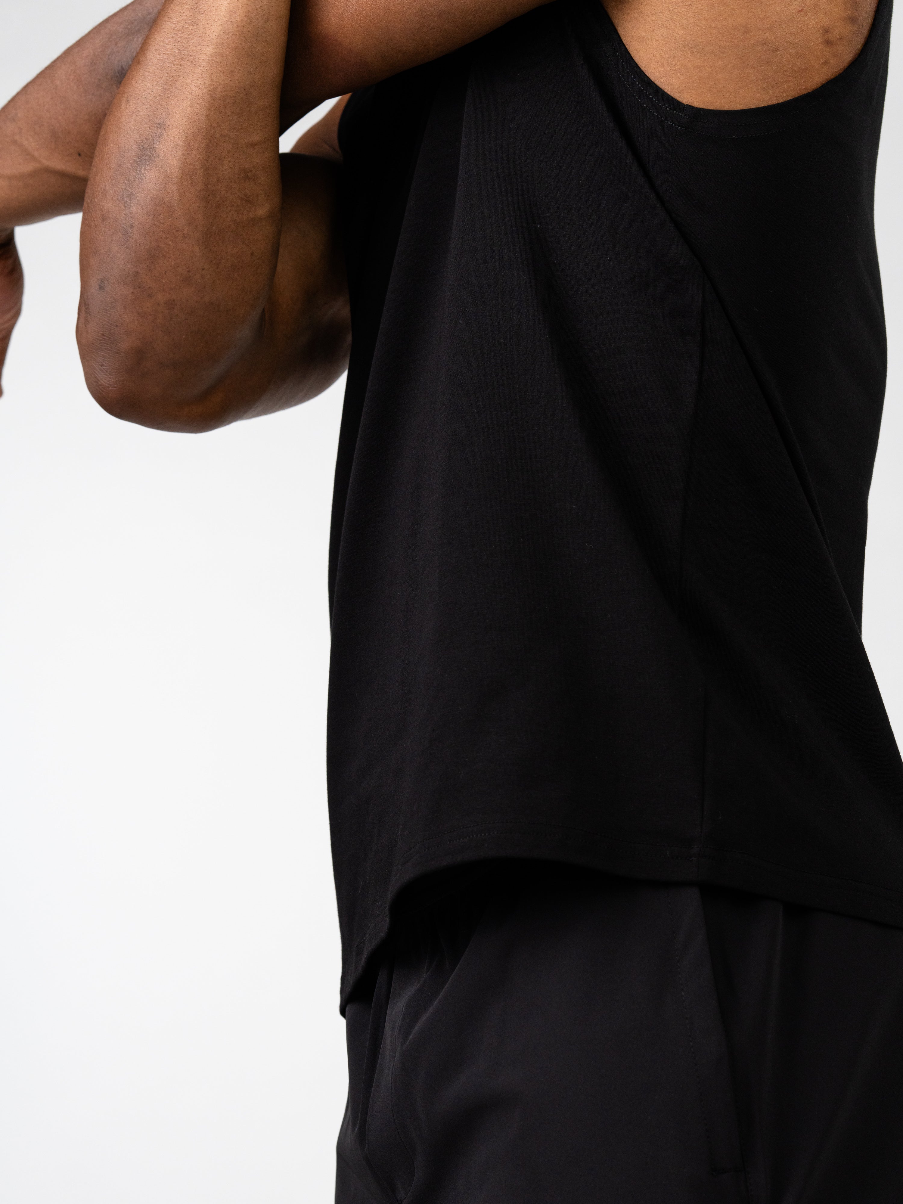 Close-up of a person wearing a black Vital Cross Sleeveless Tank, designed for high-output training and unrestricted movement, highlighting the sleeveless cut and comfortable fit.