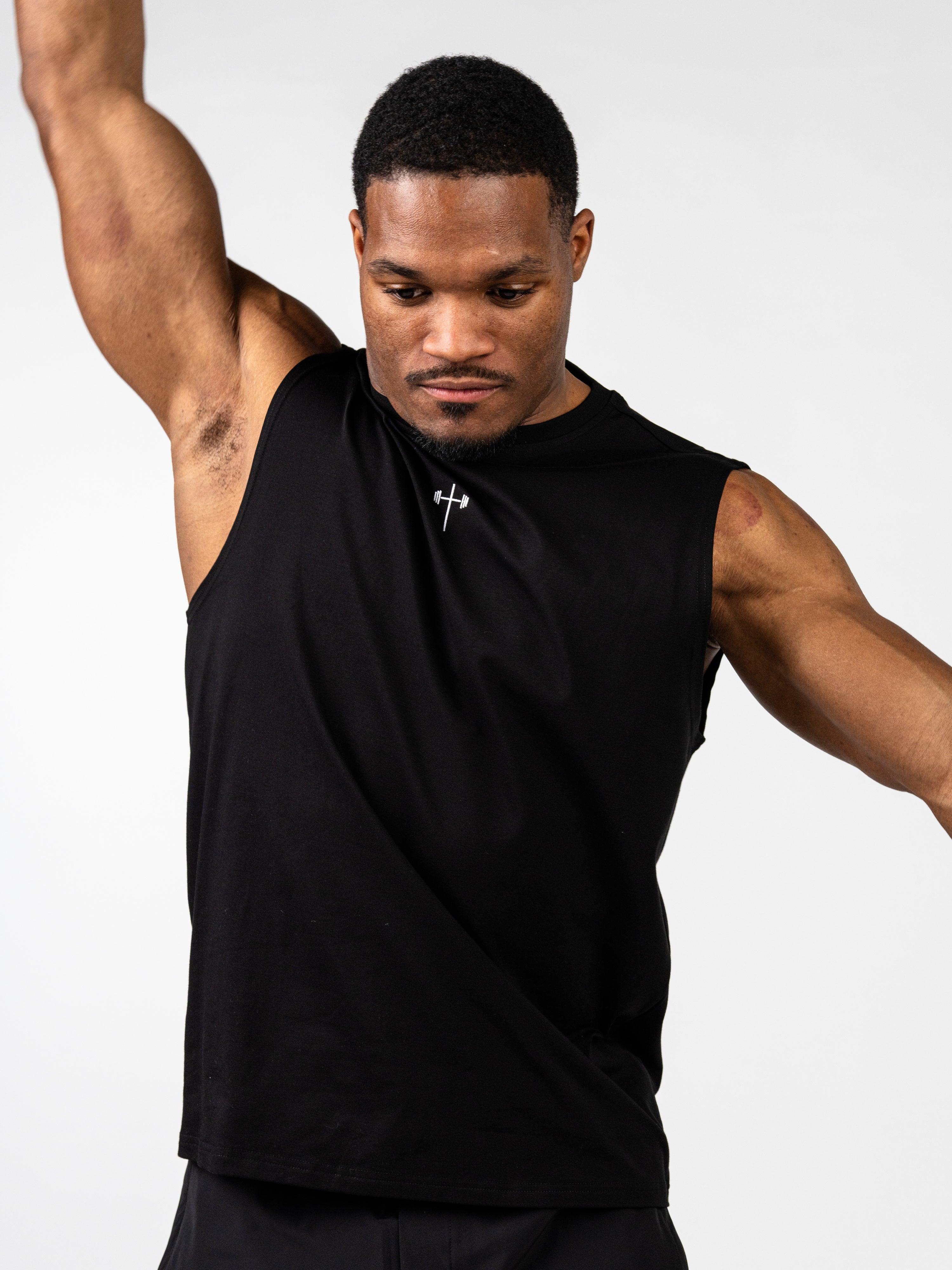 Male athlete wearing a black Vital Cross Sleeveless Tank featuring a subtle cross and barbell design on the chest, demonstrating freedom of movement during exercise.