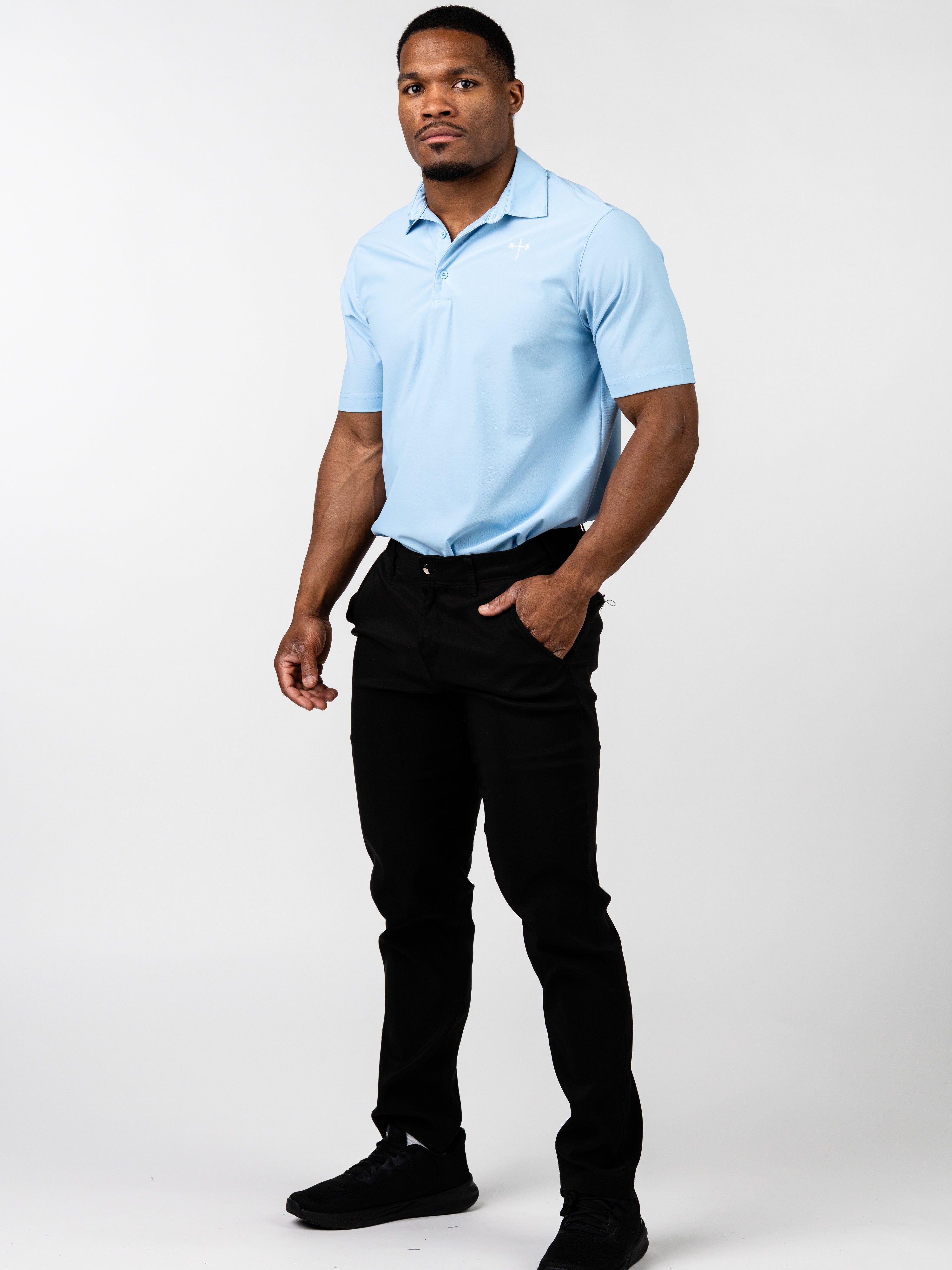 Man wearing a light blue Core Athletic Polo paired with black pants and black sneakers, standing against a plain white background in a confident pose.