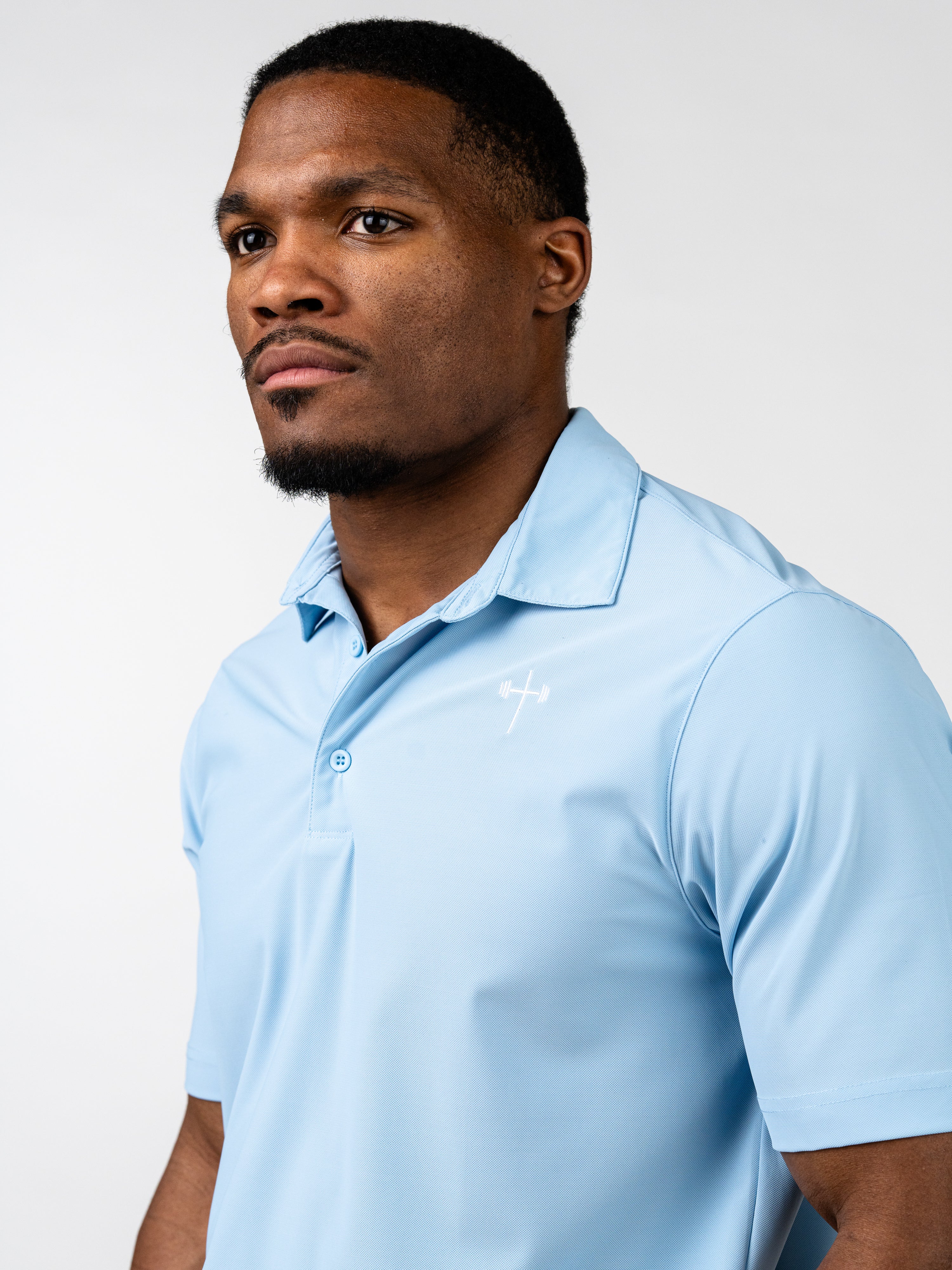 Man wearing a light blue Core Athletic Polo with a subtle cross and barbell design on the chest, showcasing Christian fitness apparel in a clean, professional style.