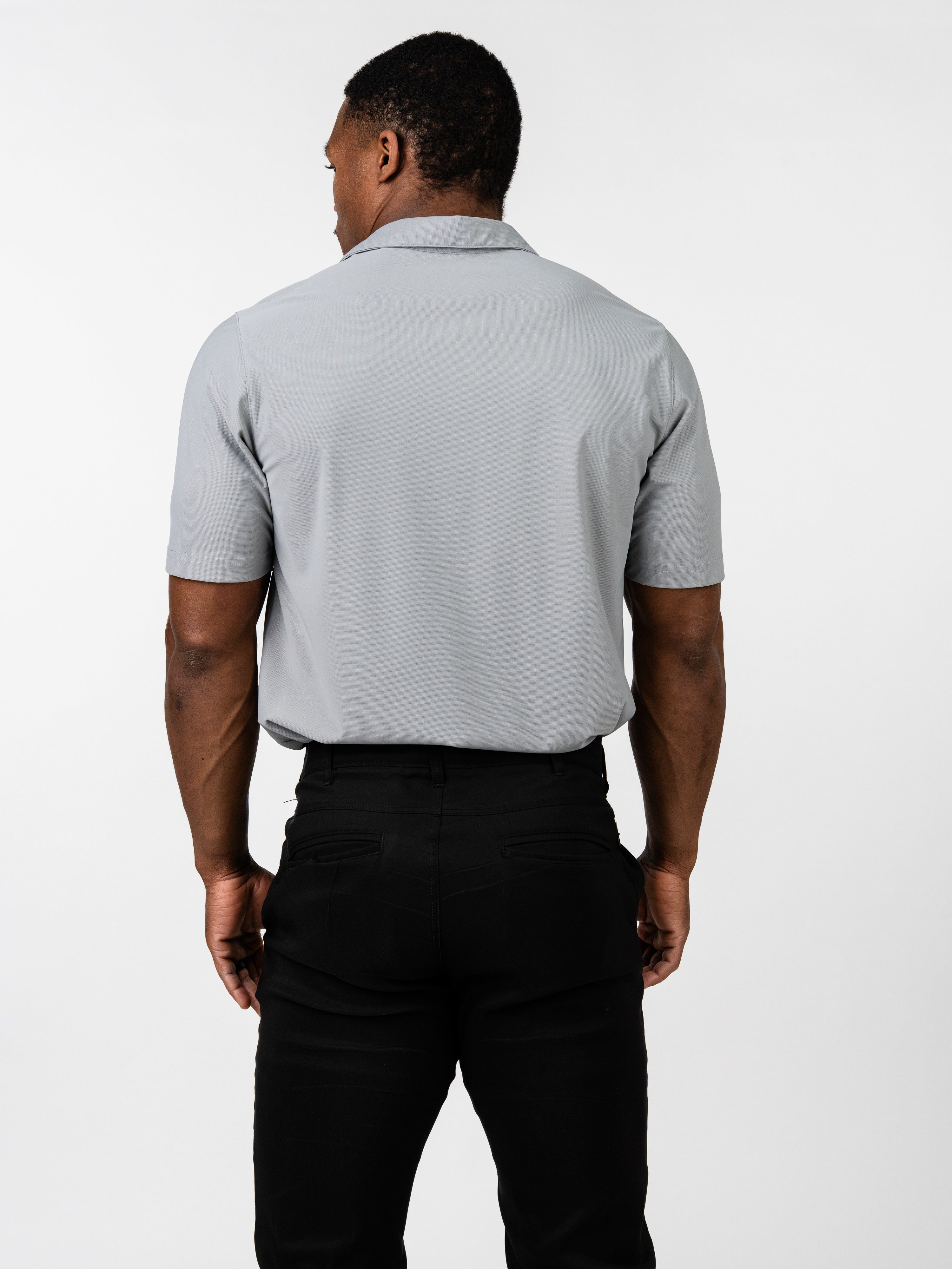 Man wearing a light gray Core Athletic Polo standing with back facing the camera, paired with black pants, showcasing the smooth, fitted fabric designed for movement and comfort.