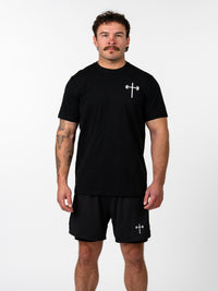 Man wearing a black Kingdom Performance Tee with a small white cross and barbell design on the chest, paired with matching black shorts featuring the same emblem, standing against a plain background.