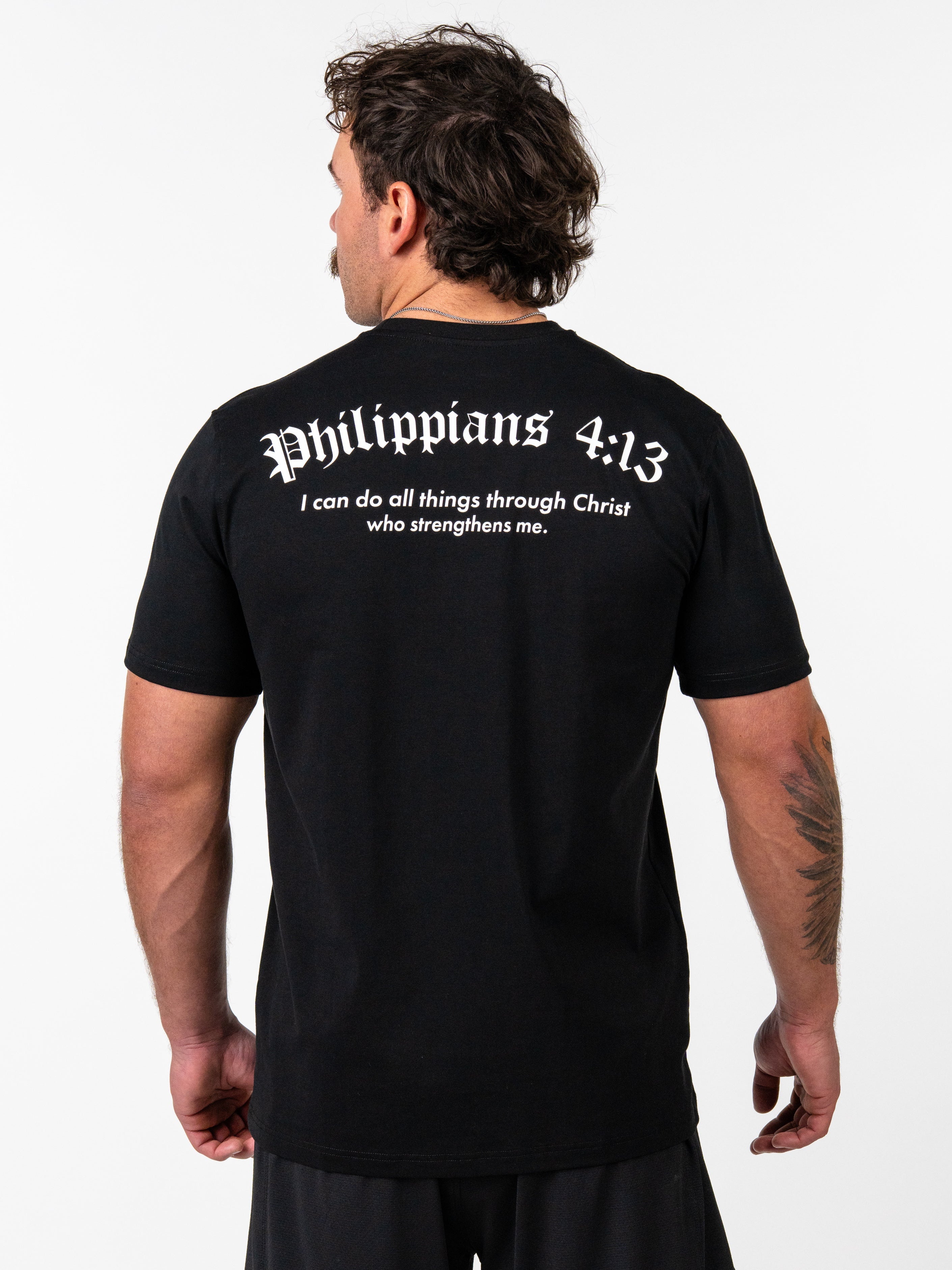 Man wearing a black Kingdom Performance Tee featuring the scripture Philippians 4:13 on the back, standing with his back to the camera against a plain white background.