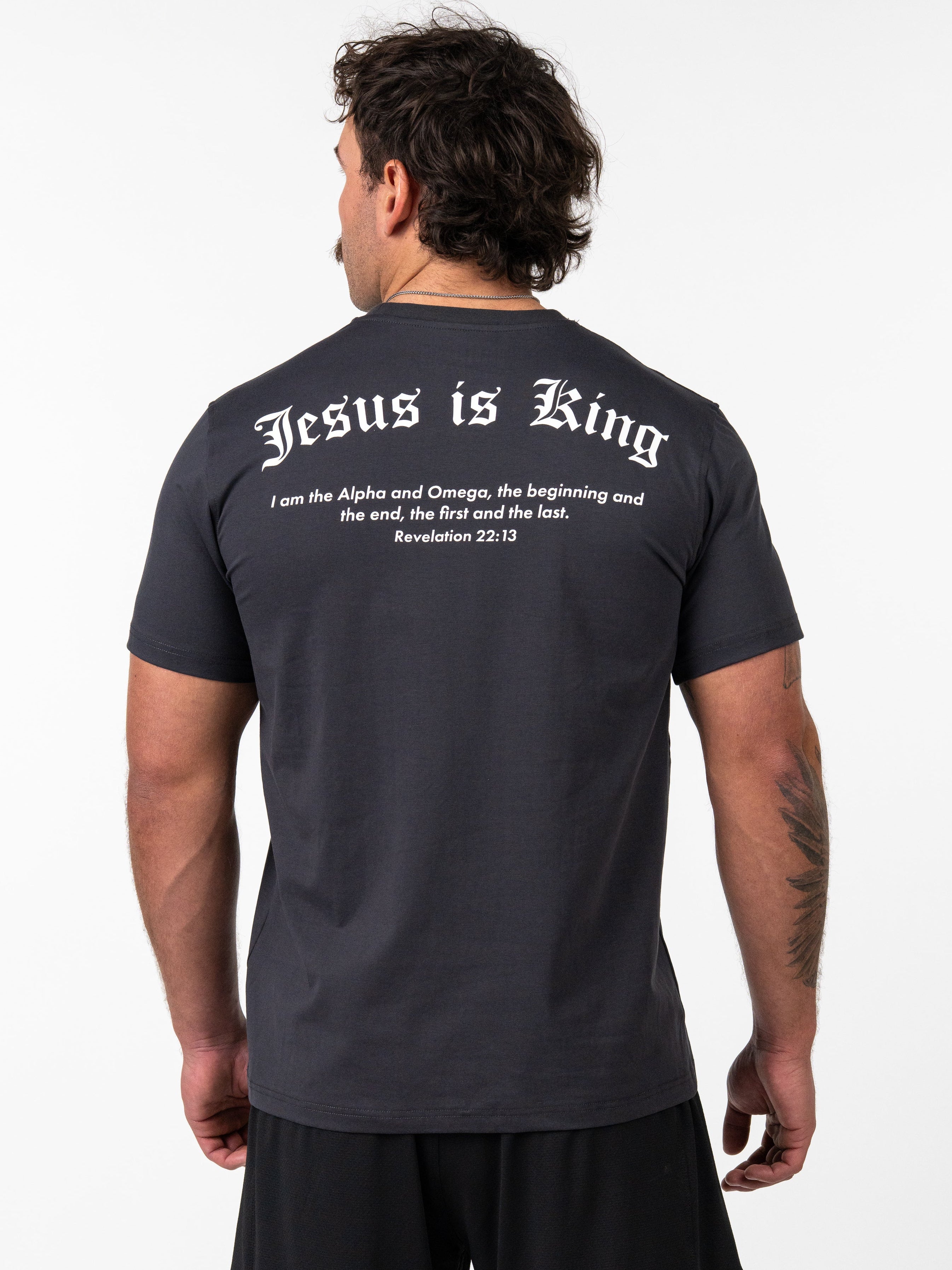 Man wearing a black Kingdom Performance Tee with the back printed text "Jesus is King" and a Bible verse from Revelation 22:13, shown in a faith-based fitness apparel style.