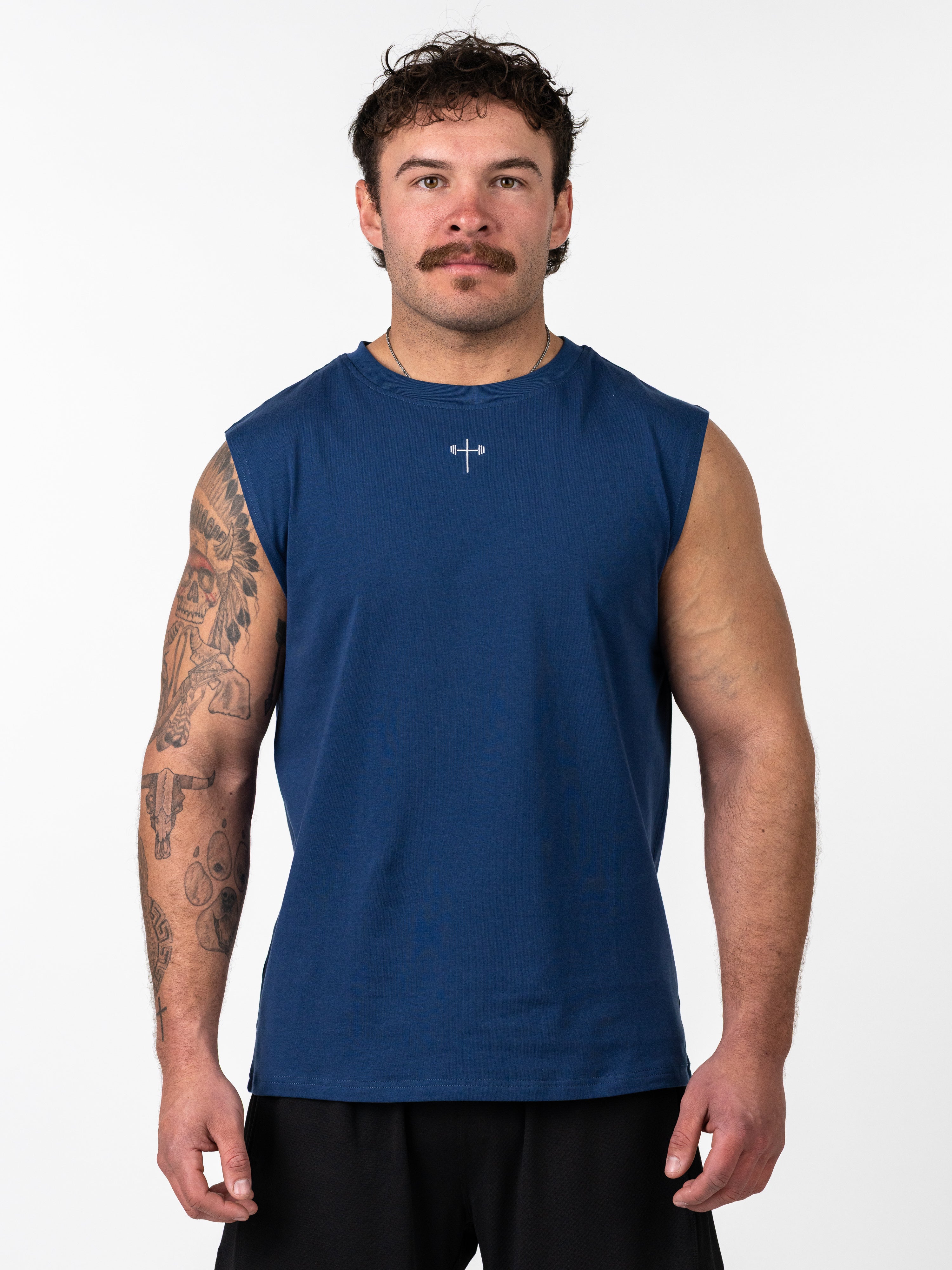Man wearing a navy blue Scripture Premium Sleeveless Tank featuring a small cross and barbell graphic on the chest, styled for Christian fitness apparel.