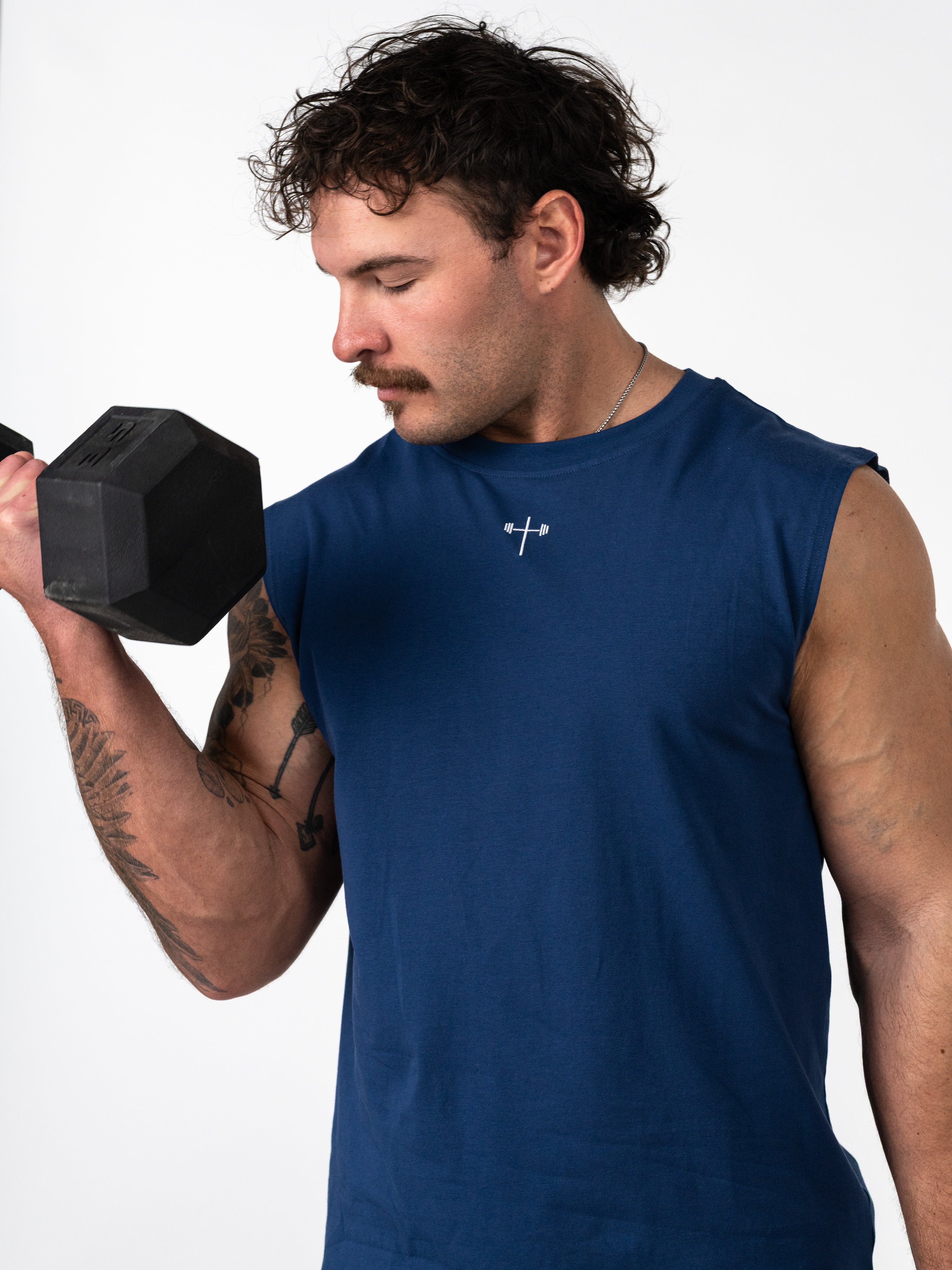 Man lifting dumbbell wearing a navy blue Scripture Premium Sleeveless Tank with a subtle cross and barbell design on the chest, representing Christian fitness apparel.