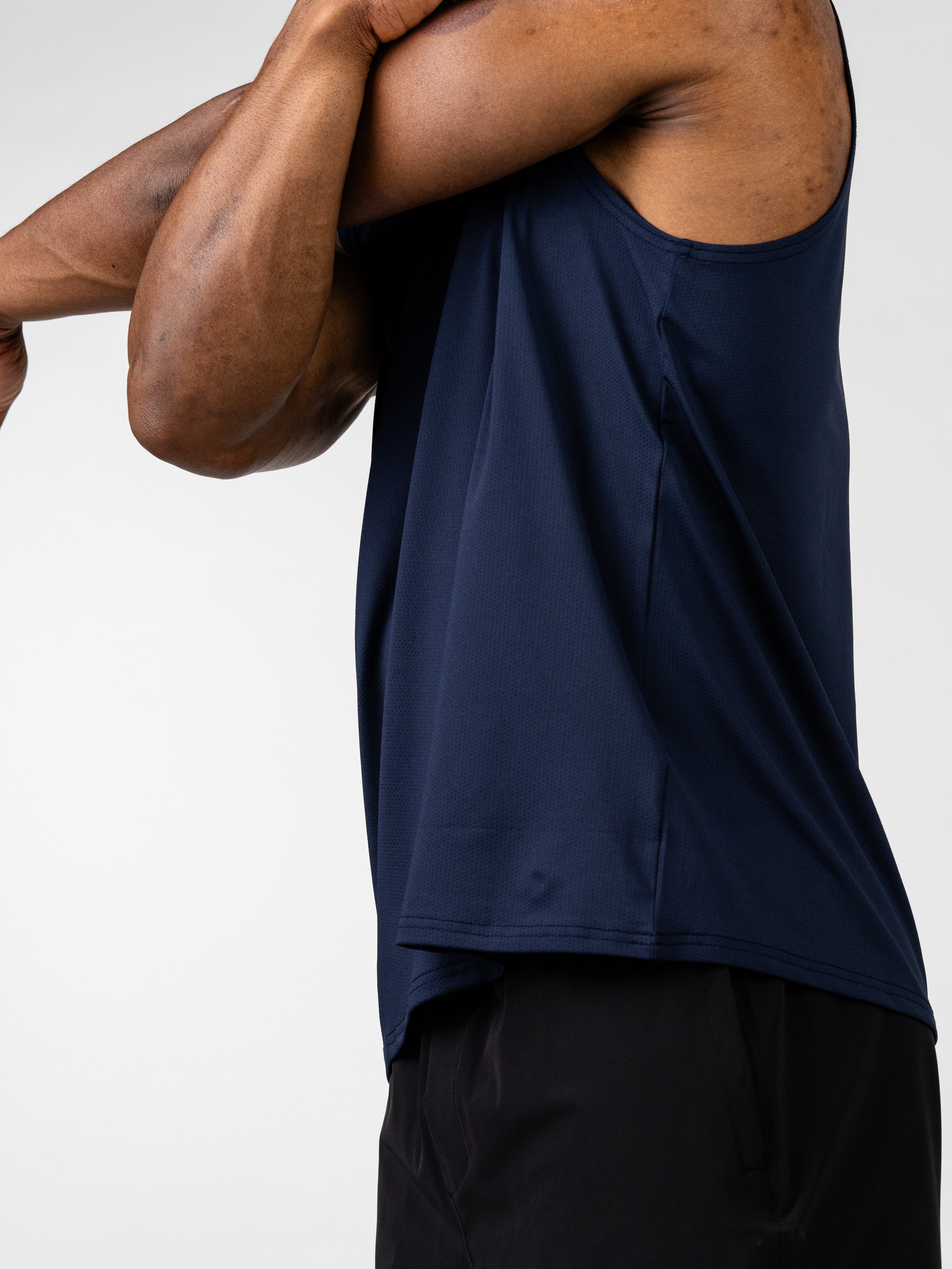 Close-up side view of a person wearing a navy blue Carry Your Cross Premium Oversized Tank while stretching their arm, highlighting the relaxed fit and breathable fabric of the Christian gym clothing.