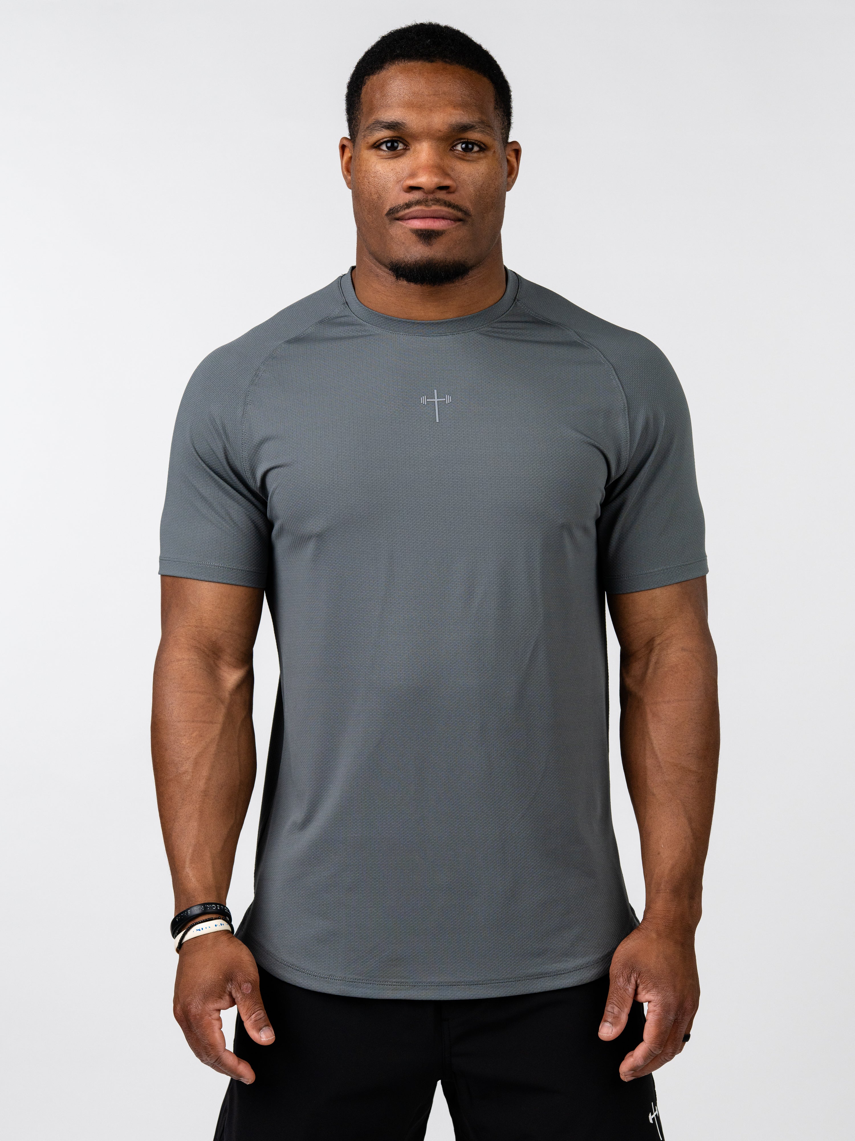 Man wearing a fitted gray Signature Tee with a small cross design on the chest, made from breathable performance fabric suitable for intense training and activewear.