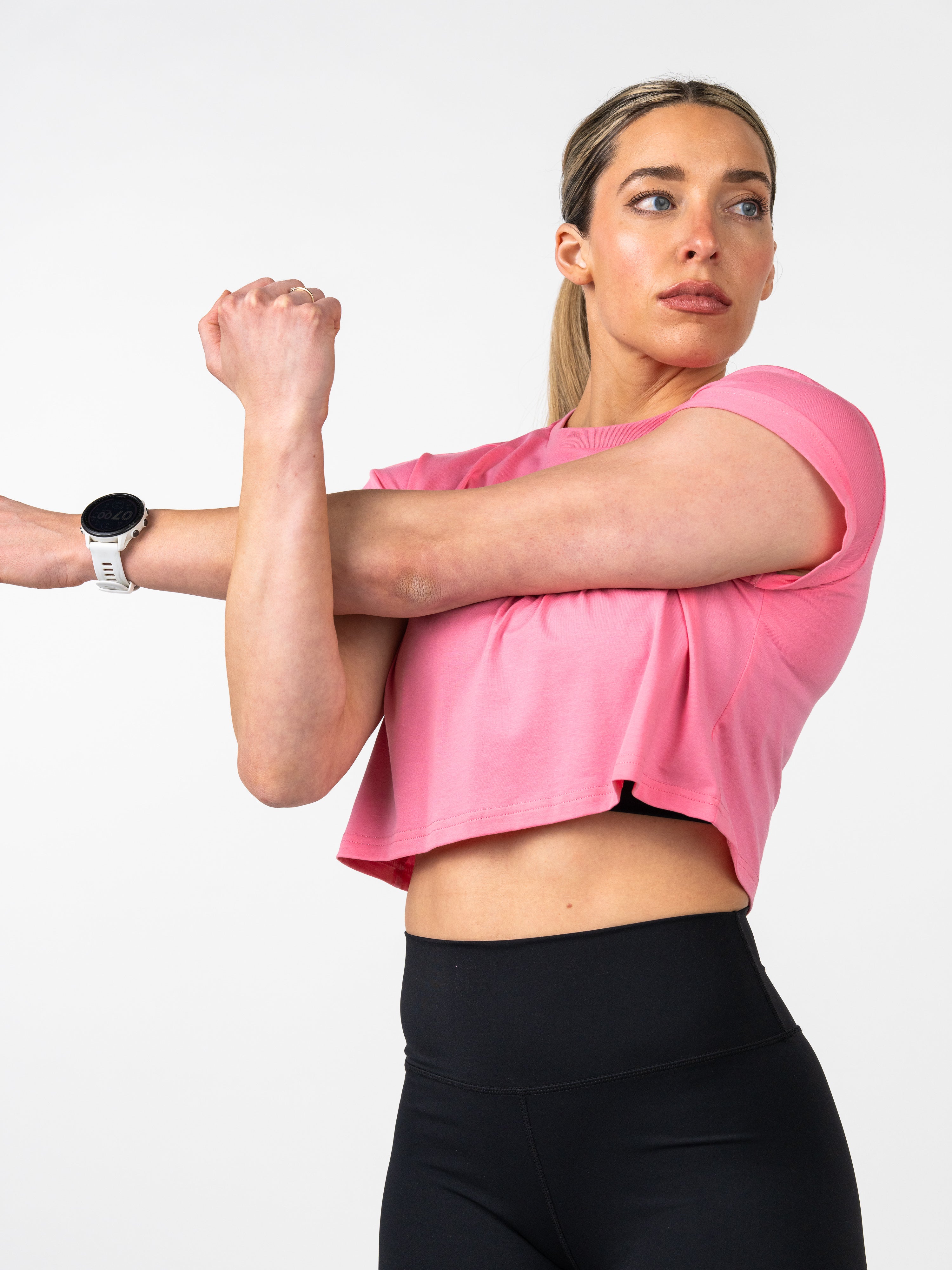 Woman wearing a pink Cross Essential Crop Tee stretching her arm across her chest, demonstrating comfortable, performance-focused Christian fitness apparel.