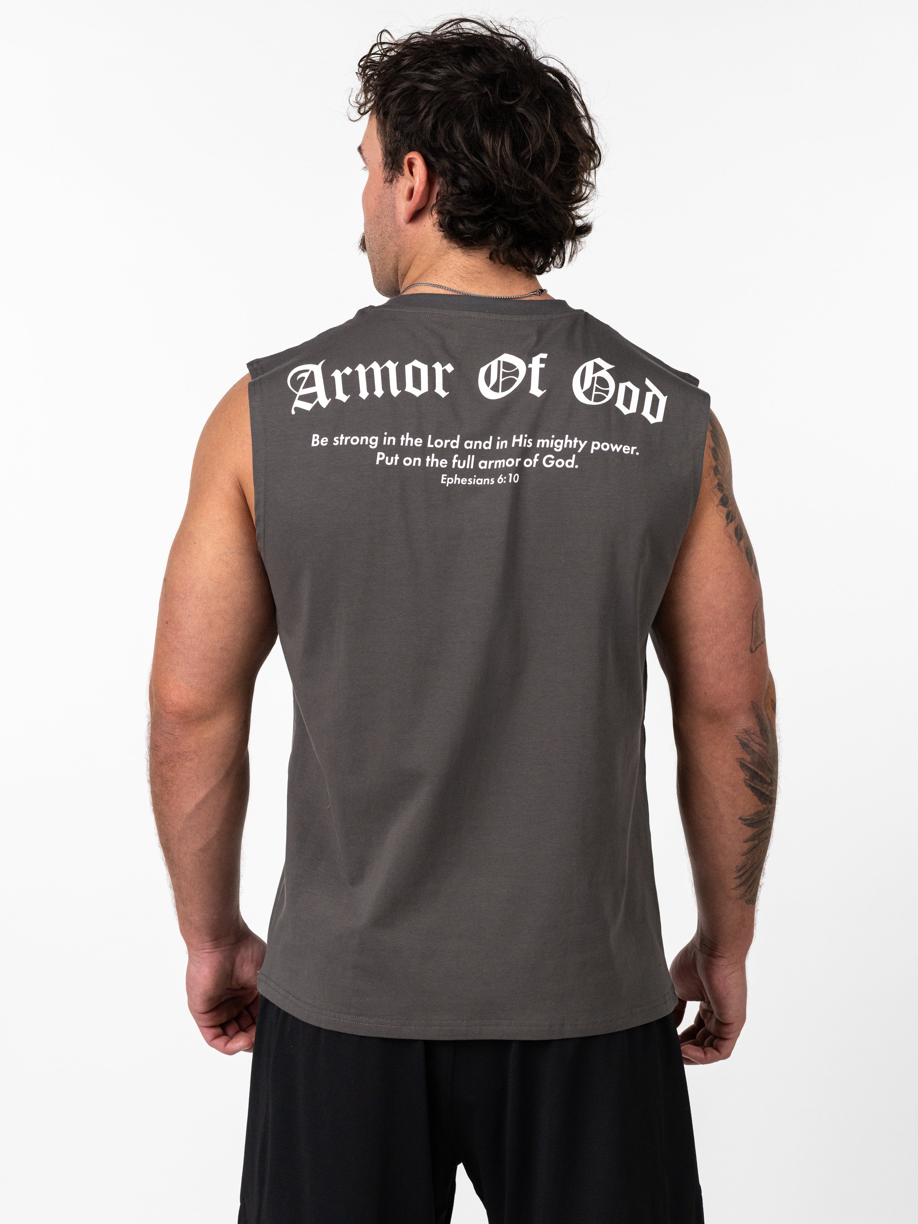 Man wearing a dark gray Scripture Premium Sleeveless Tank with "Armor Of God" and a Bible verse printed on the back, standing against a white background.