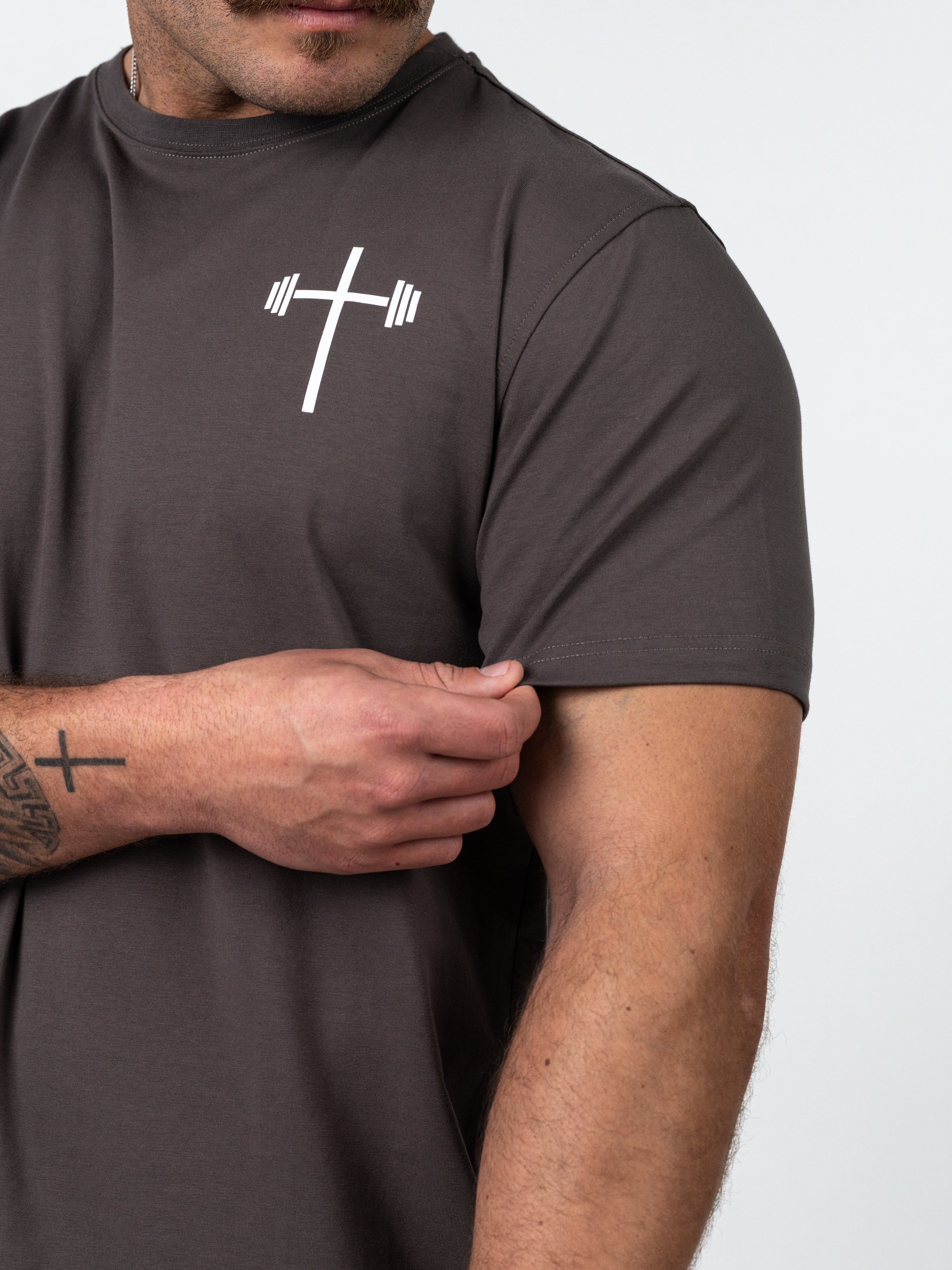 Close-up of a man wearing a dark grey Kingdom Performance Tee featuring a white cross combined with a barbell design on the chest, highlighting Christian fitness apparel.