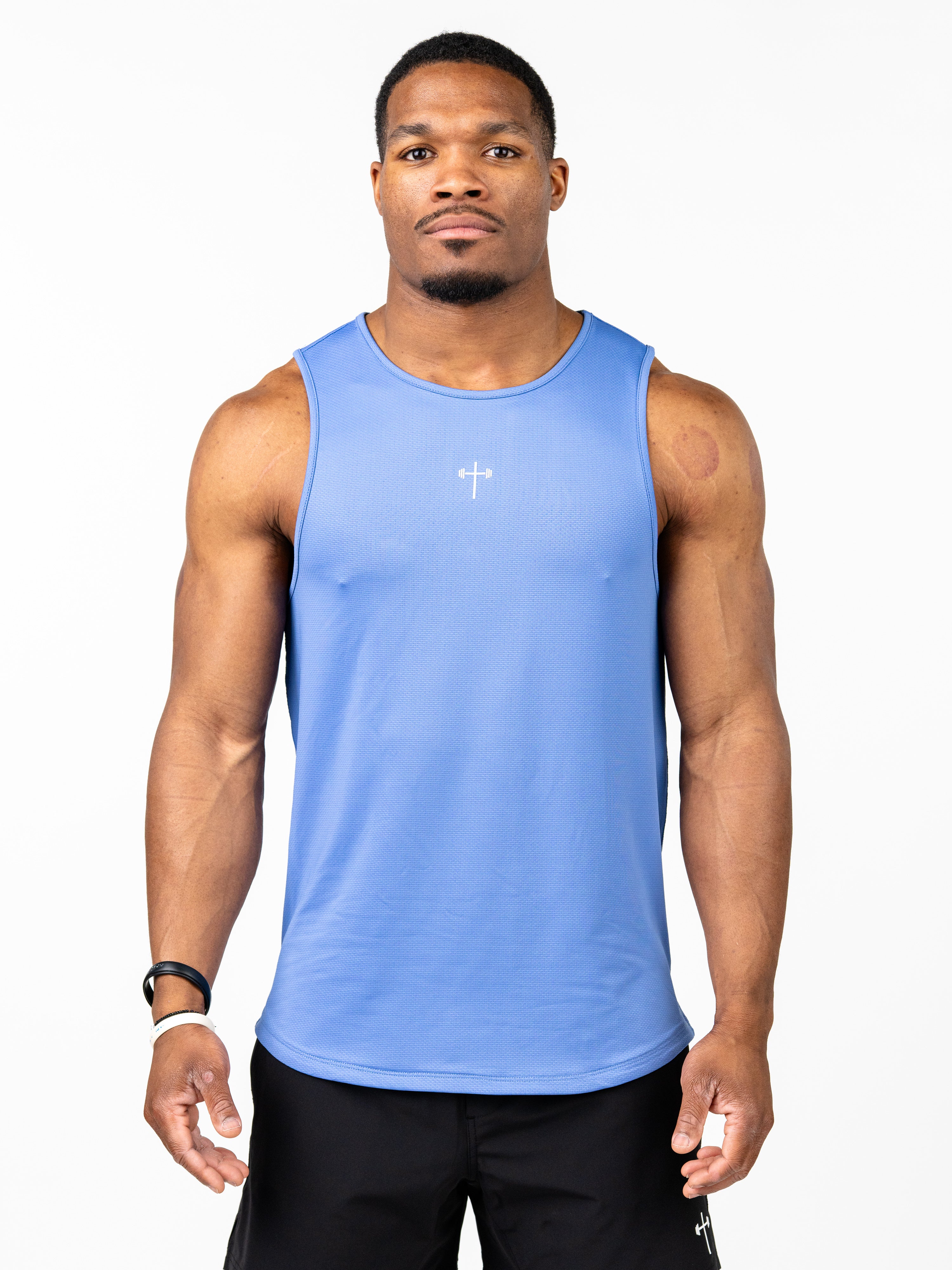 Man wearing a blue Signature Tank with a small white cross and barbell design on the chest, paired with black shorts, showcasing breathable, performance Christian gym clothing.