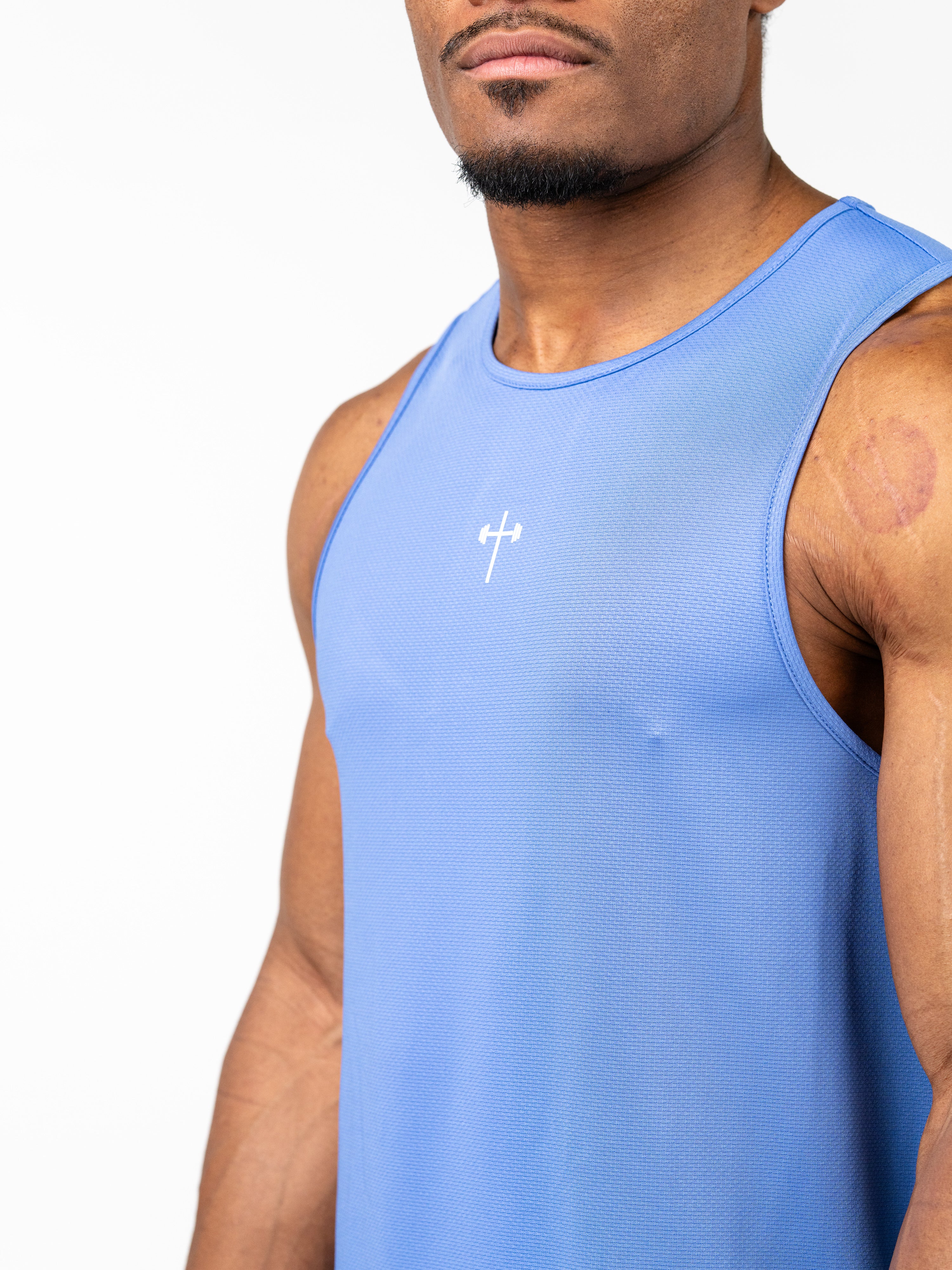 Athletic man wearing a blue Signature Tank designed for intense training, featuring a small white Christian cross with a barbell icon on the chest, made from breathable performance fabric.