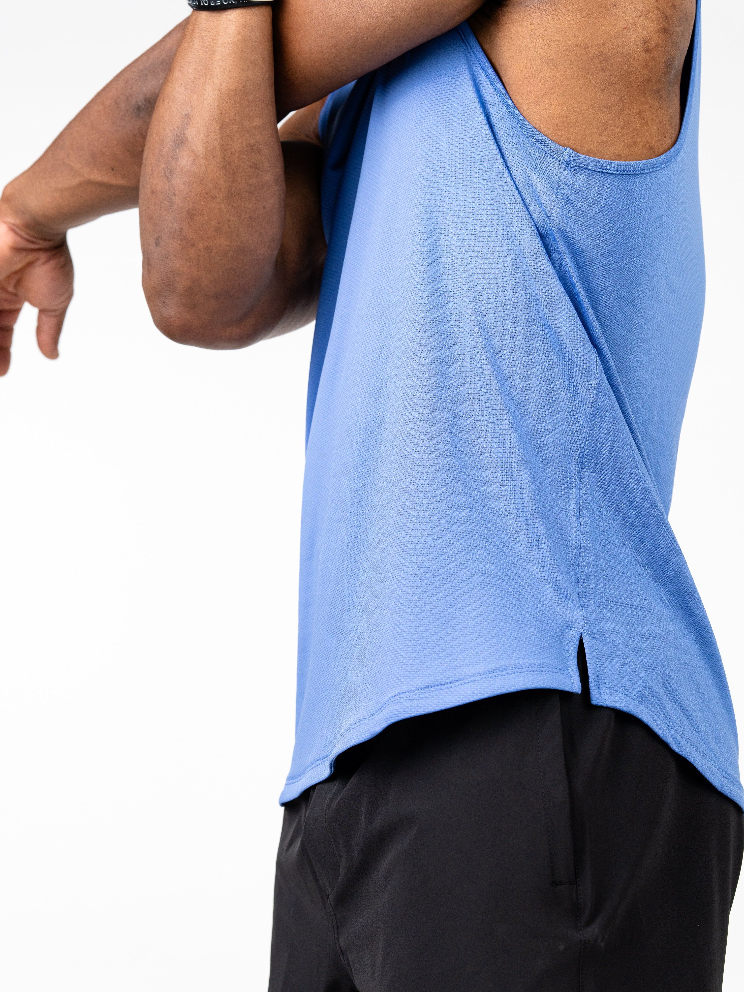 Close-up side view of a person stretching wearing a blue Signature Tank made from breathable, four-way stretch fabric designed for intense training and sweat-wicking performance.