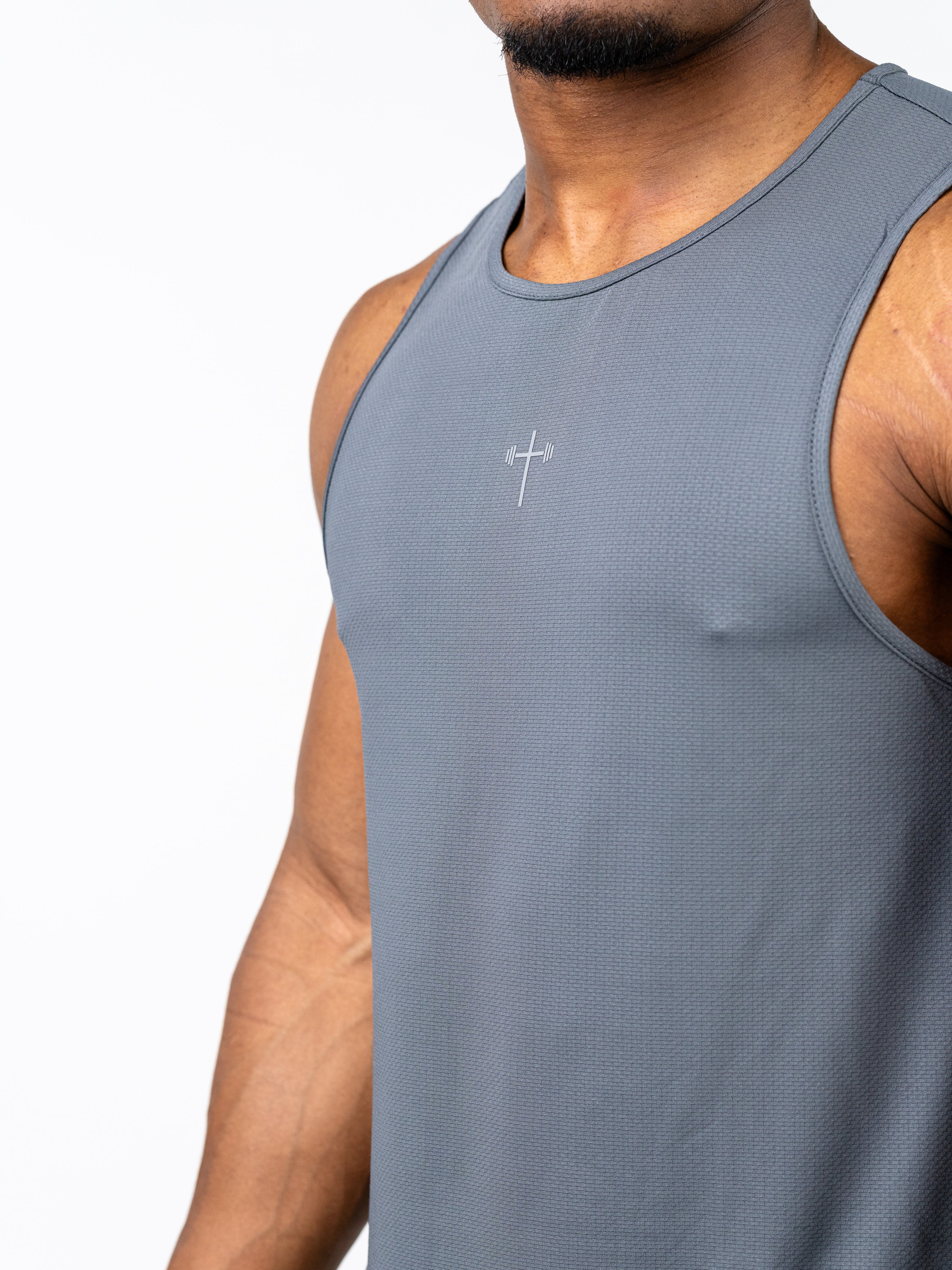 Close-up of a man wearing a gray Signature Tank featuring a subtle cross with a barbell design, made from breathable, sweat-wicking fabric for Christian fitness apparel.
