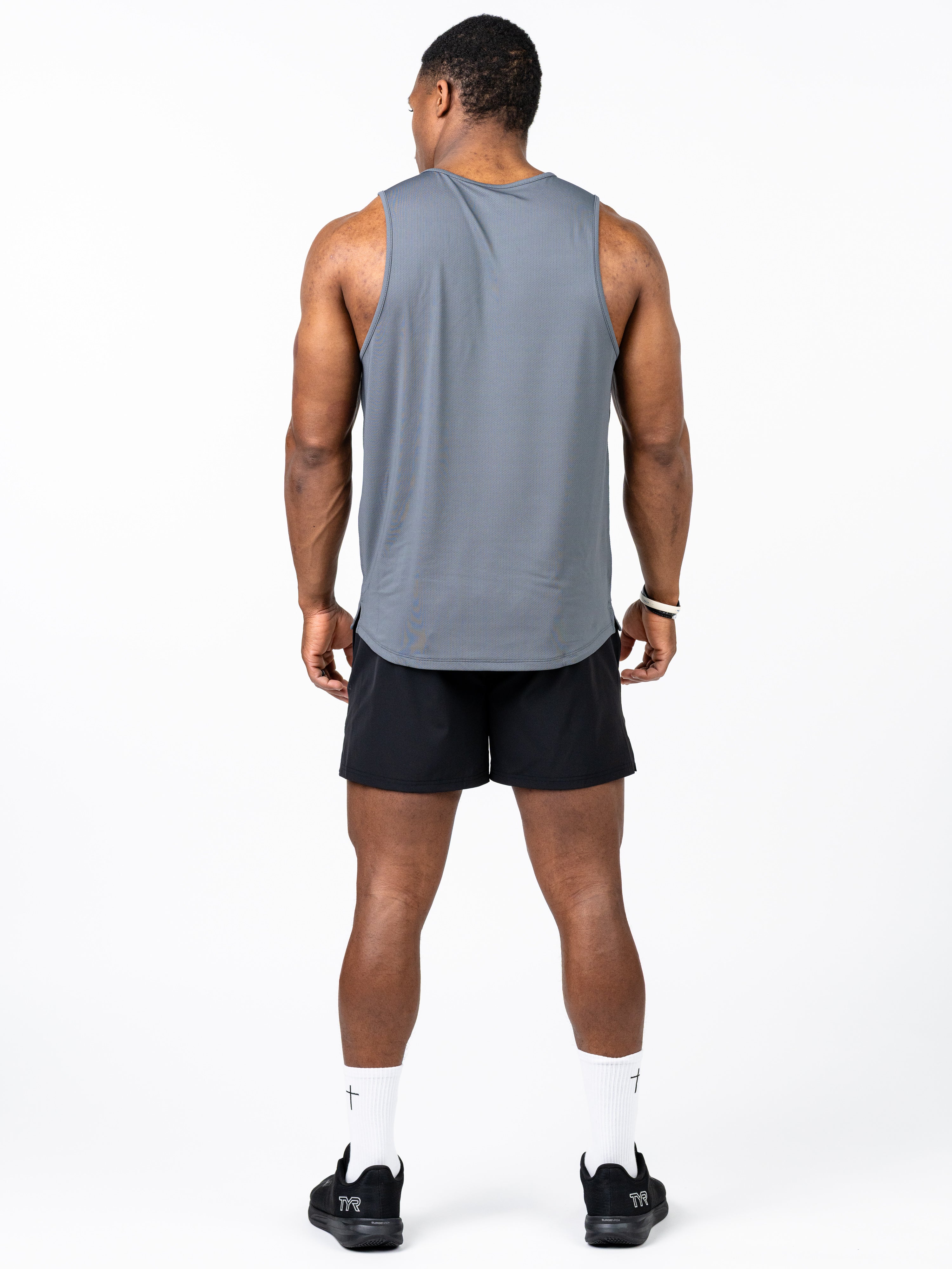 Rear view of a man wearing a gray Signature Tank made from breathable, stretch performance fabric paired with black shorts and white socks featuring a subtle cross design, representing Christian fitness apparel.