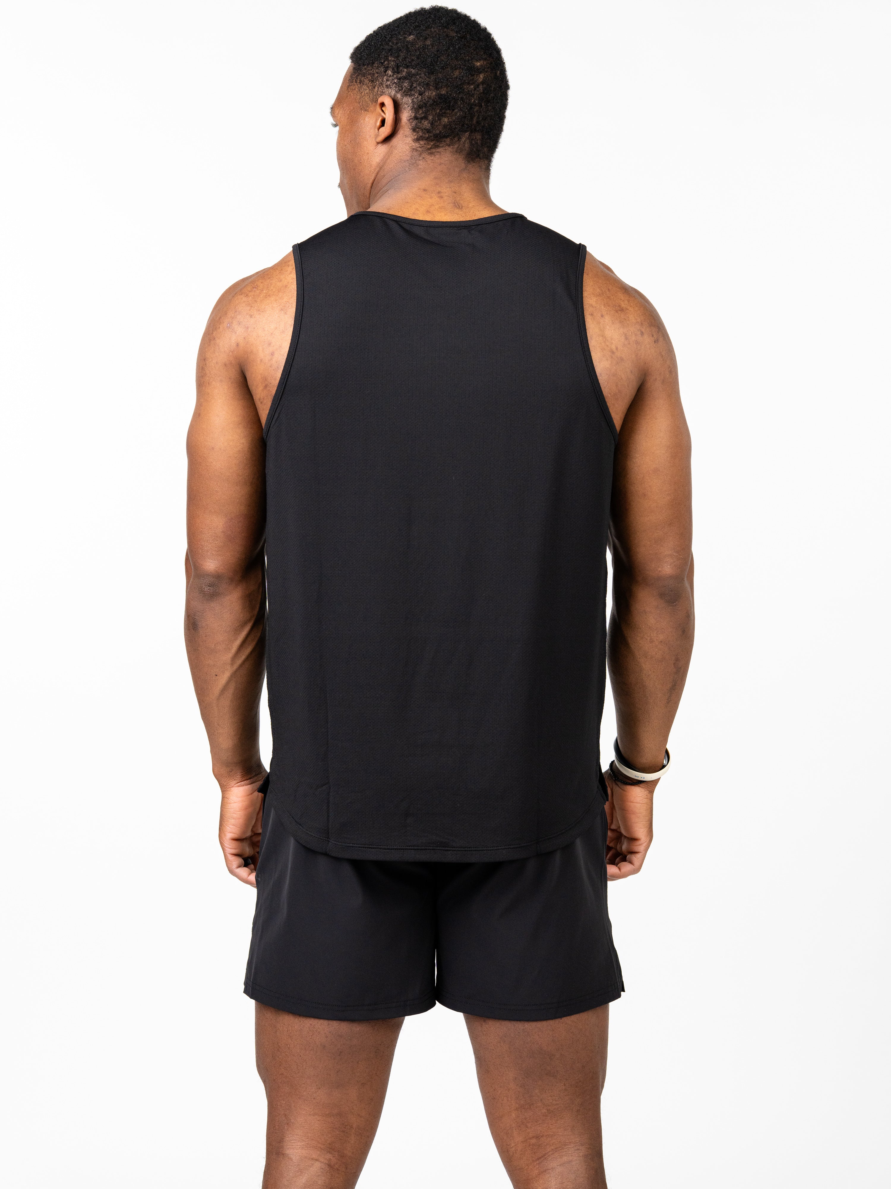 Man wearing a black Signature Tank, standing with back to camera in a plain white studio, dressed in black athletic shorts showcasing breathable, 4-way stretch performance fabric suitable for intense training.