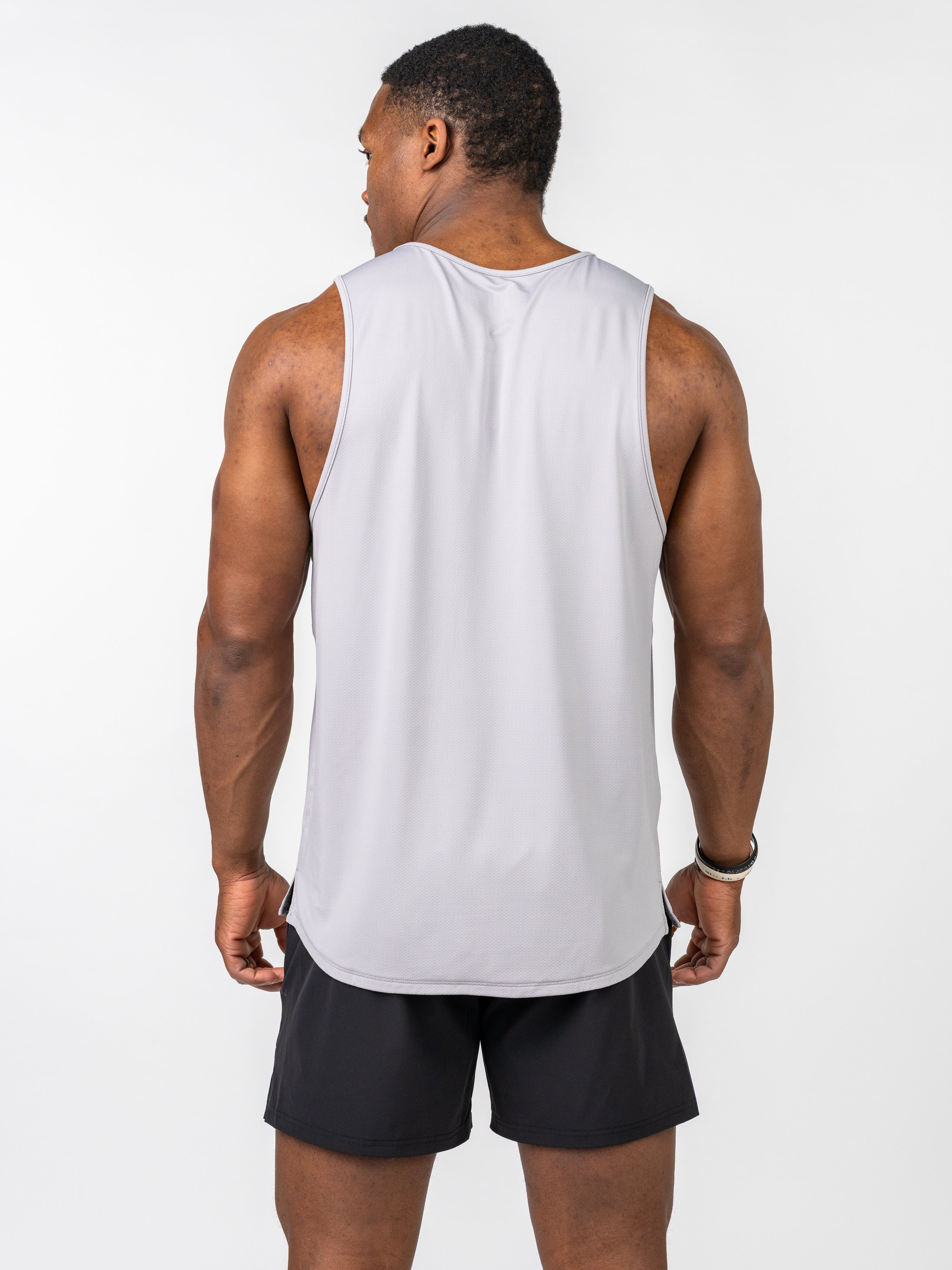 Athletic man wearing a light grey Signature Tank made from breathable, stretch fabric designed for intense training, shown from the back with black shorts.
