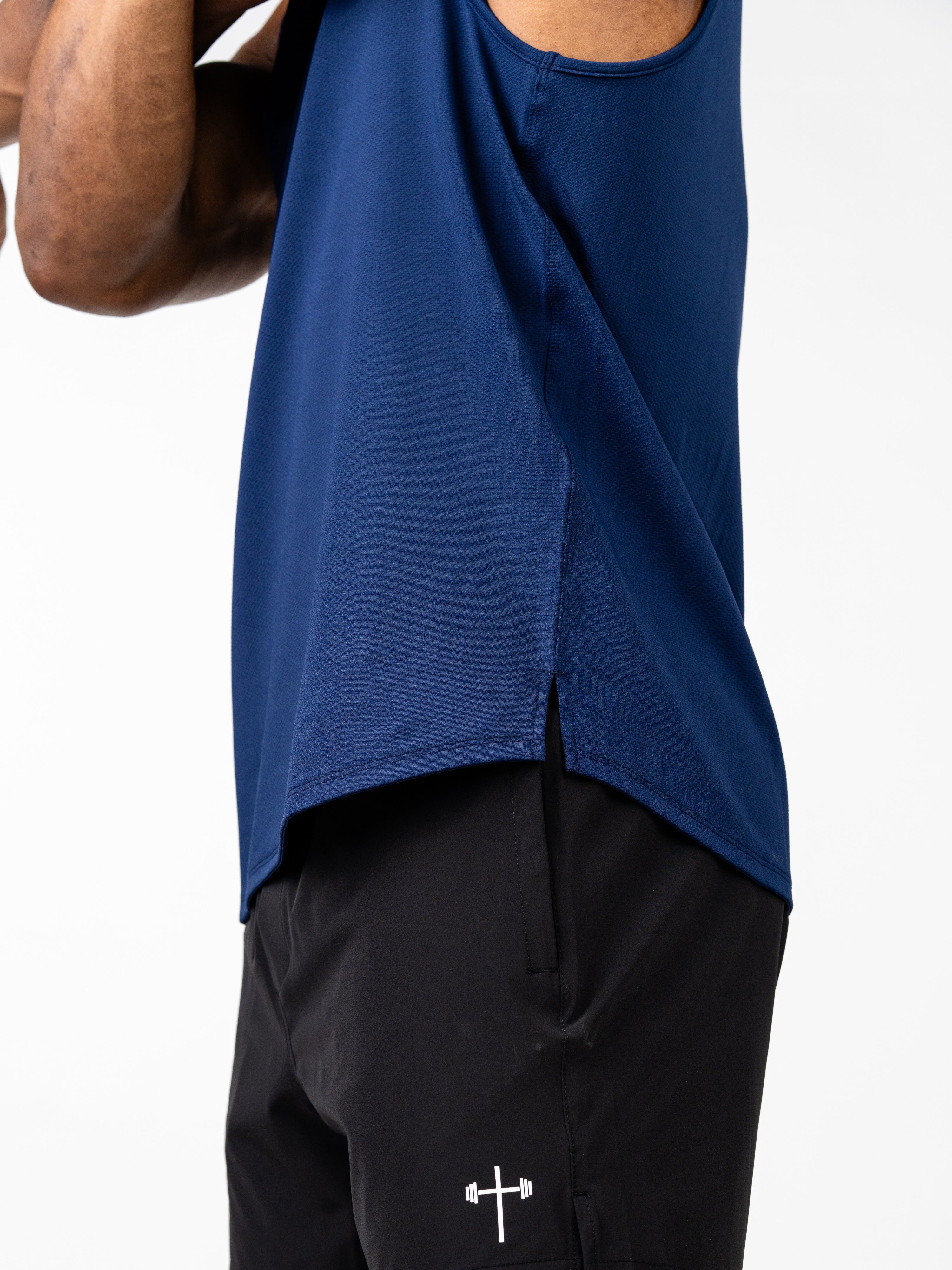 Side view of a person wearing a navy blue Signature Tank paired with black shorts featuring a small white barbell cross logo, showcasing breathable Christian fitness apparel designed for performance.