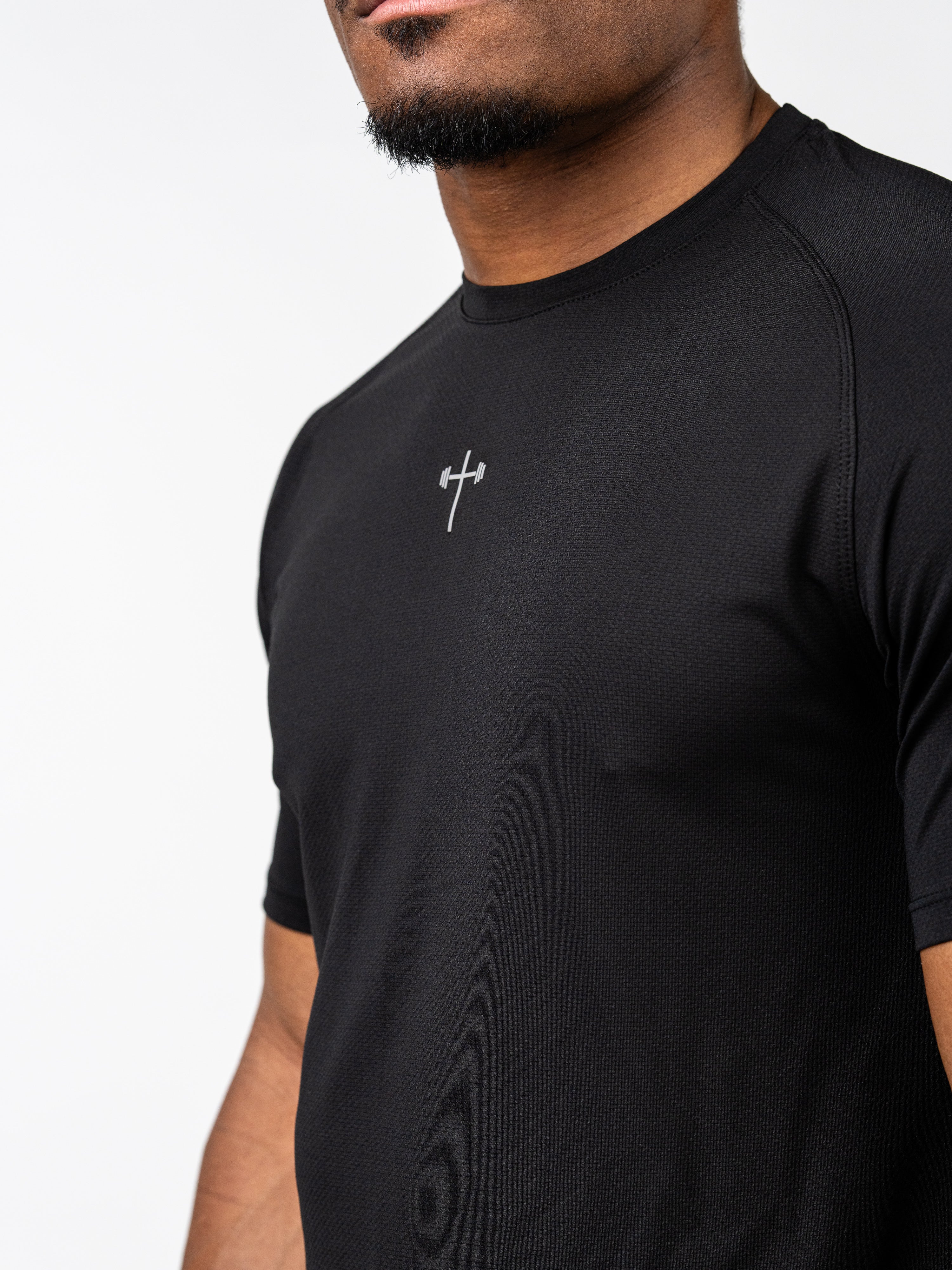 Man wearing a black Signature Tee featuring a small Christian cross with a barbell design on the chest, made from breathable, moisture-wicking performance fabric.