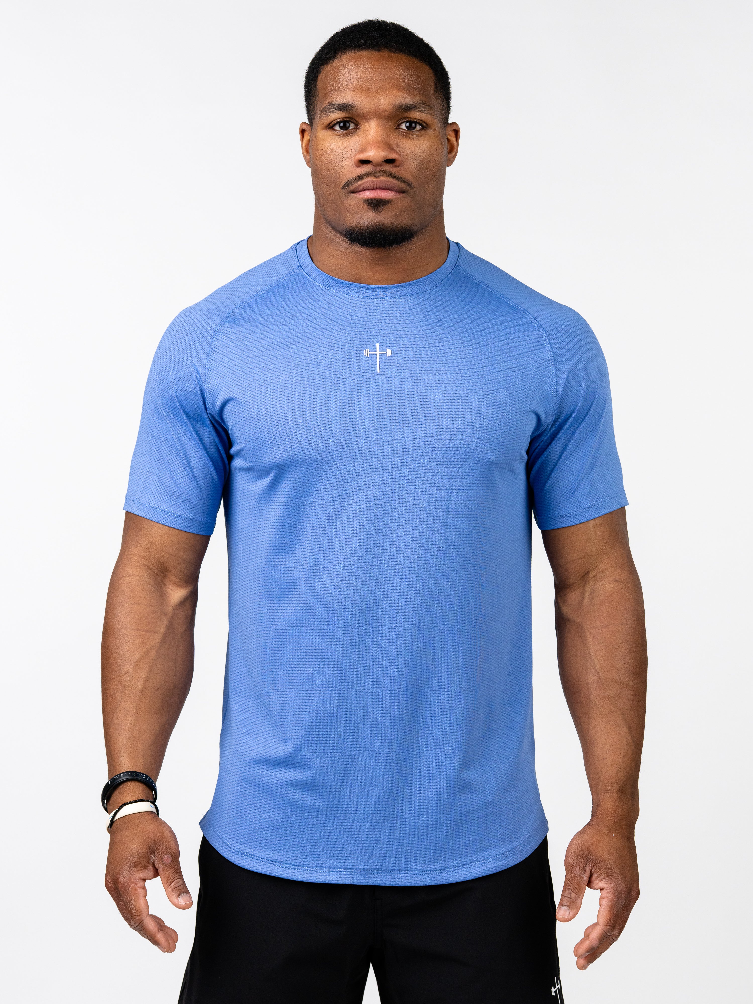 Male model wearing a blue Signature Tee with a small white cross and barbell design on the chest, showcasing breathable, performance-driven Christian fitness apparel.