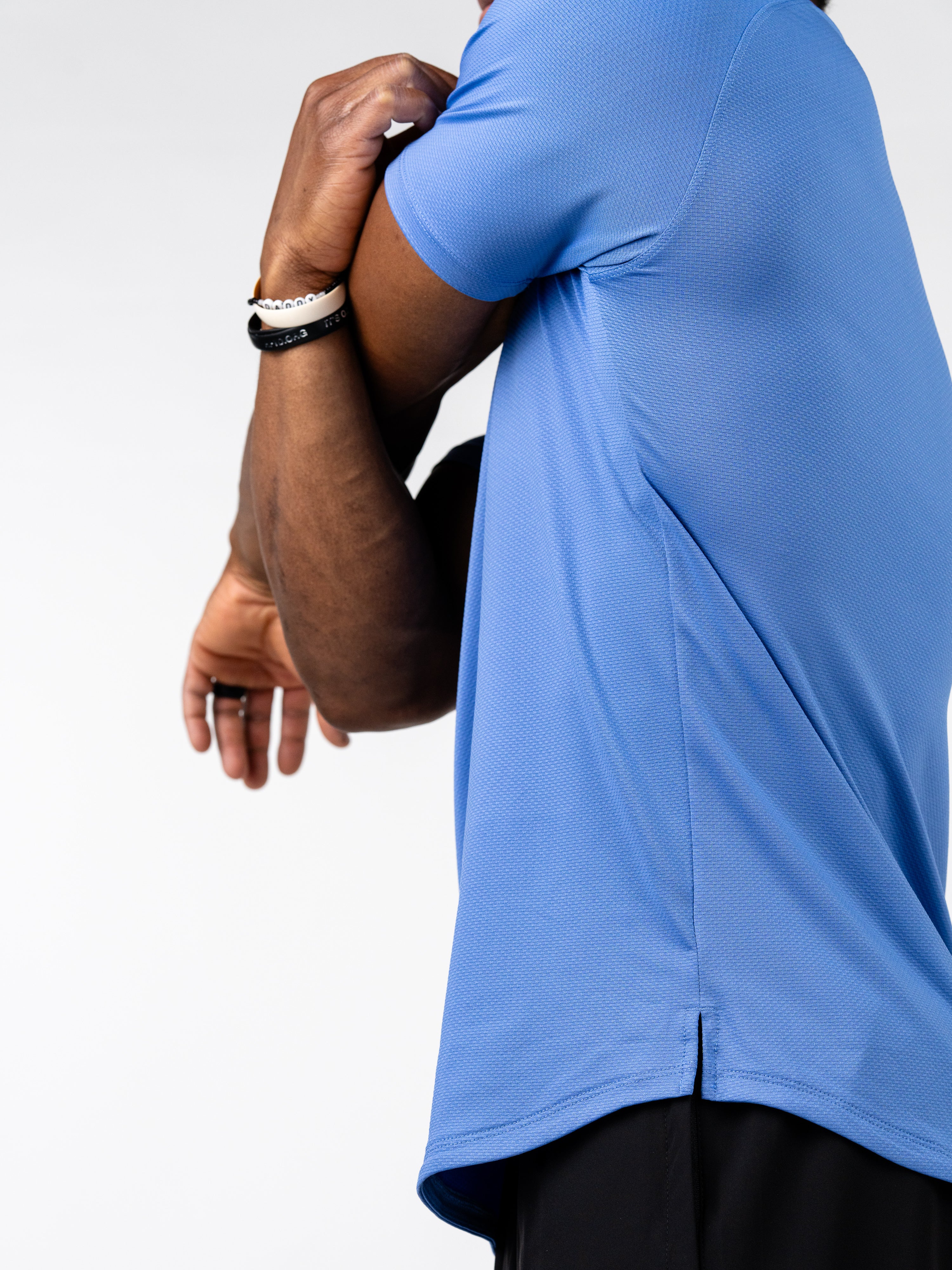 Close-up of a person stretching their arm while wearing a blue Signature Tee made from breathable, sweat-wicking fabric designed for intense training and movement.