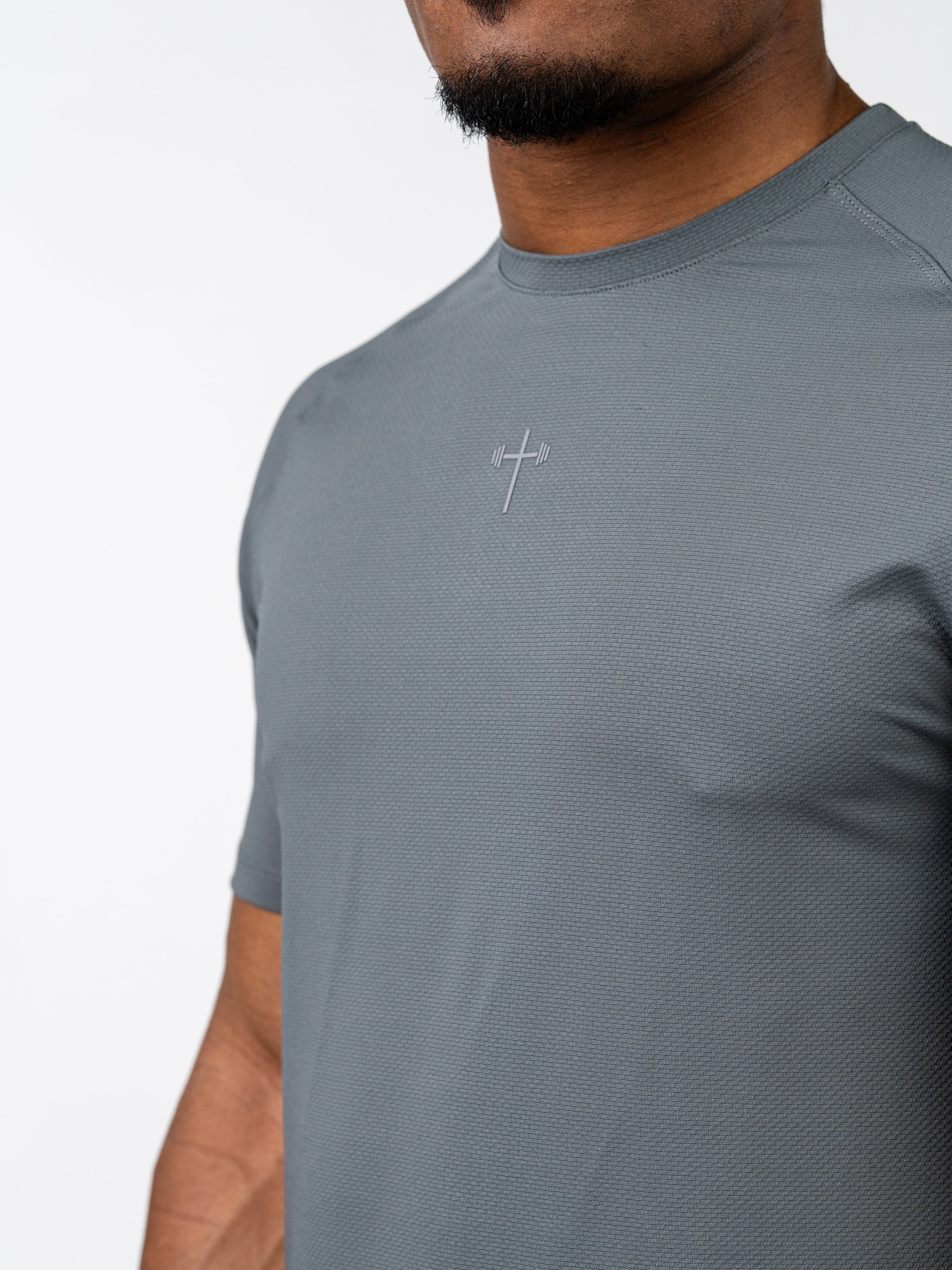 Close-up of a man wearing a grey Signature Tee featuring a subtle cross and barbell emblem on the chest, designed as breathable Christian gym clothing for performance and comfort.