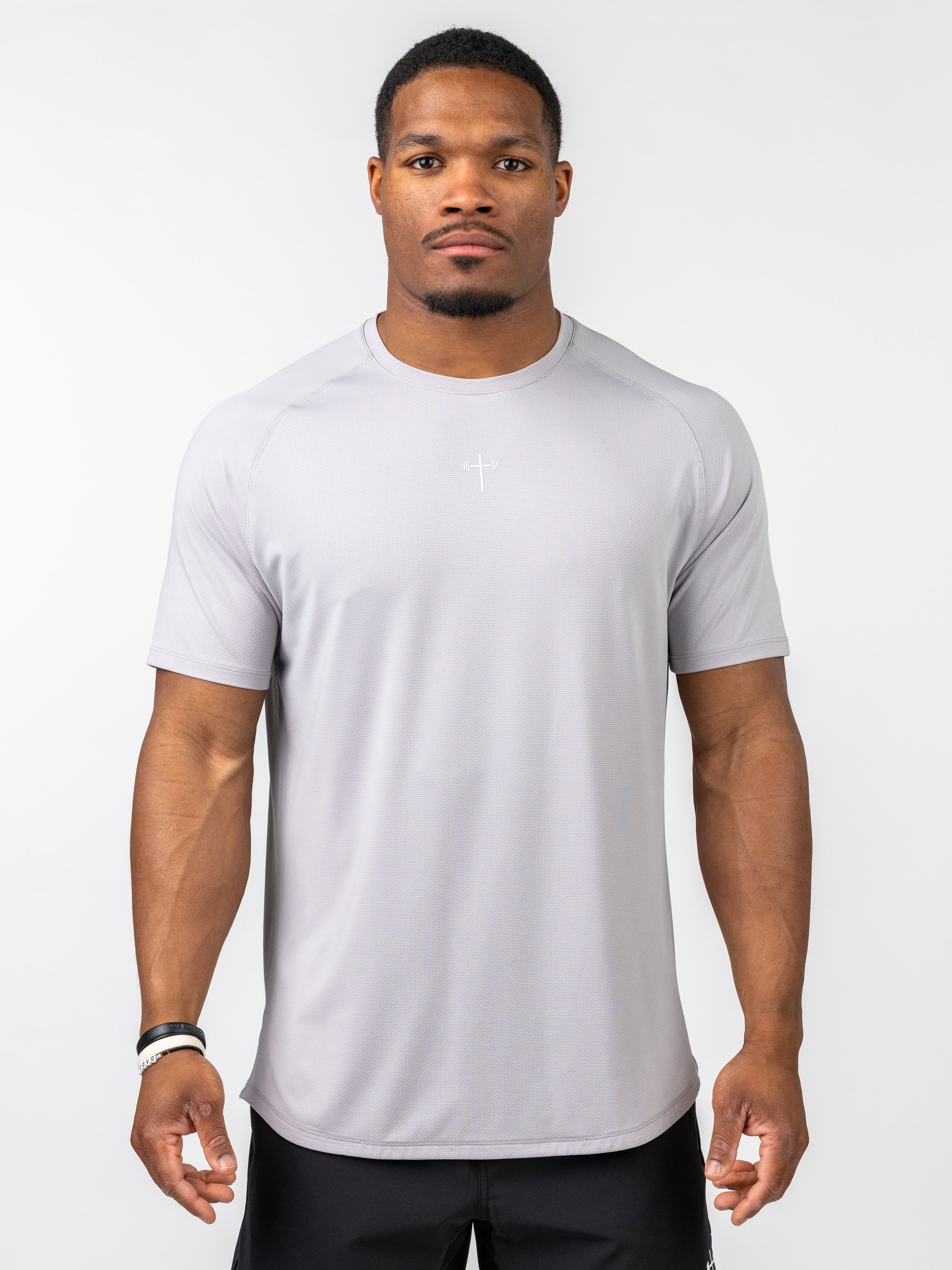 A muscular man wearing a light grey Signature Tee with a subtle white cross and barbell design on the chest, designed for performance and intense training in Christian gym clothing.