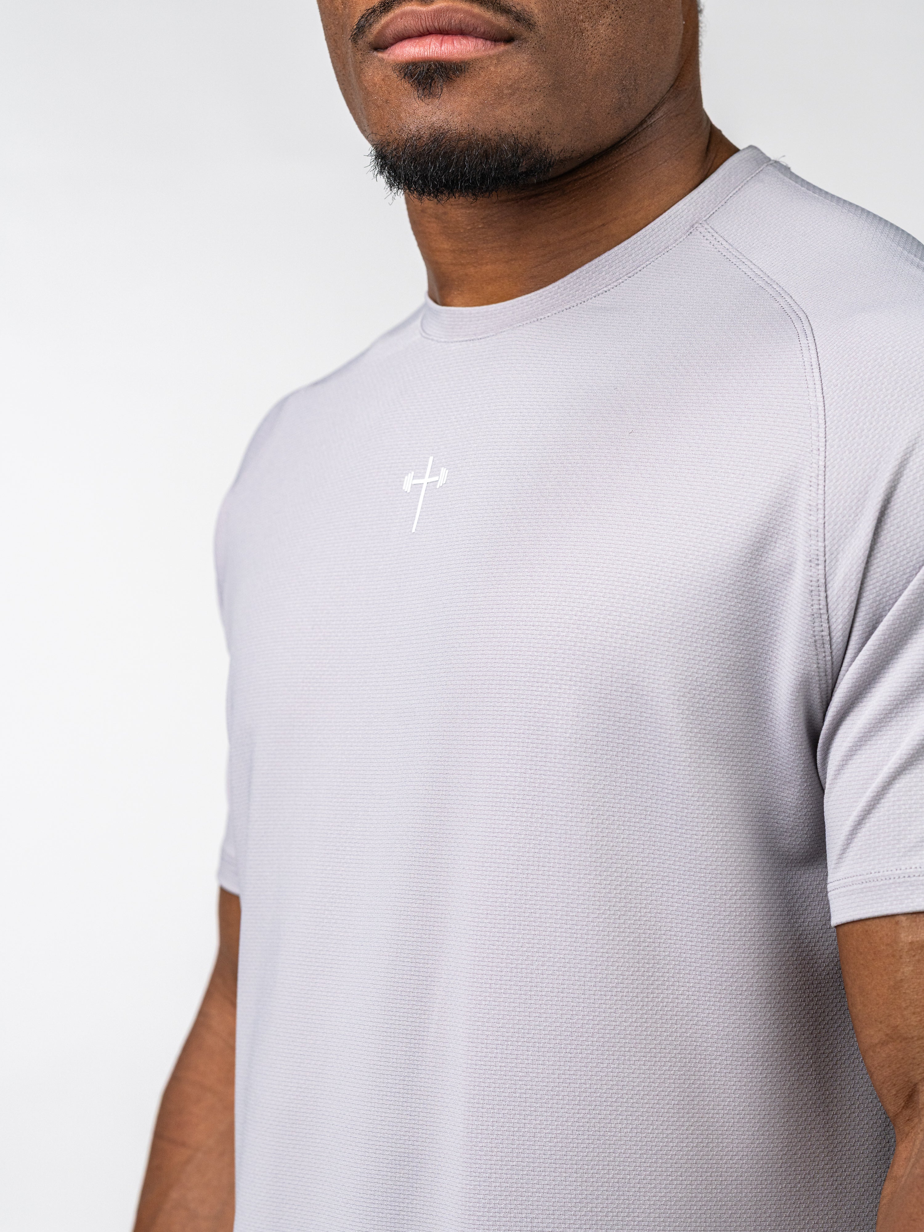 Man wearing a light grey Signature Tee featuring a subtle Christian cross with a barbell design, made from breathable, sweat-wicking performance fabric.