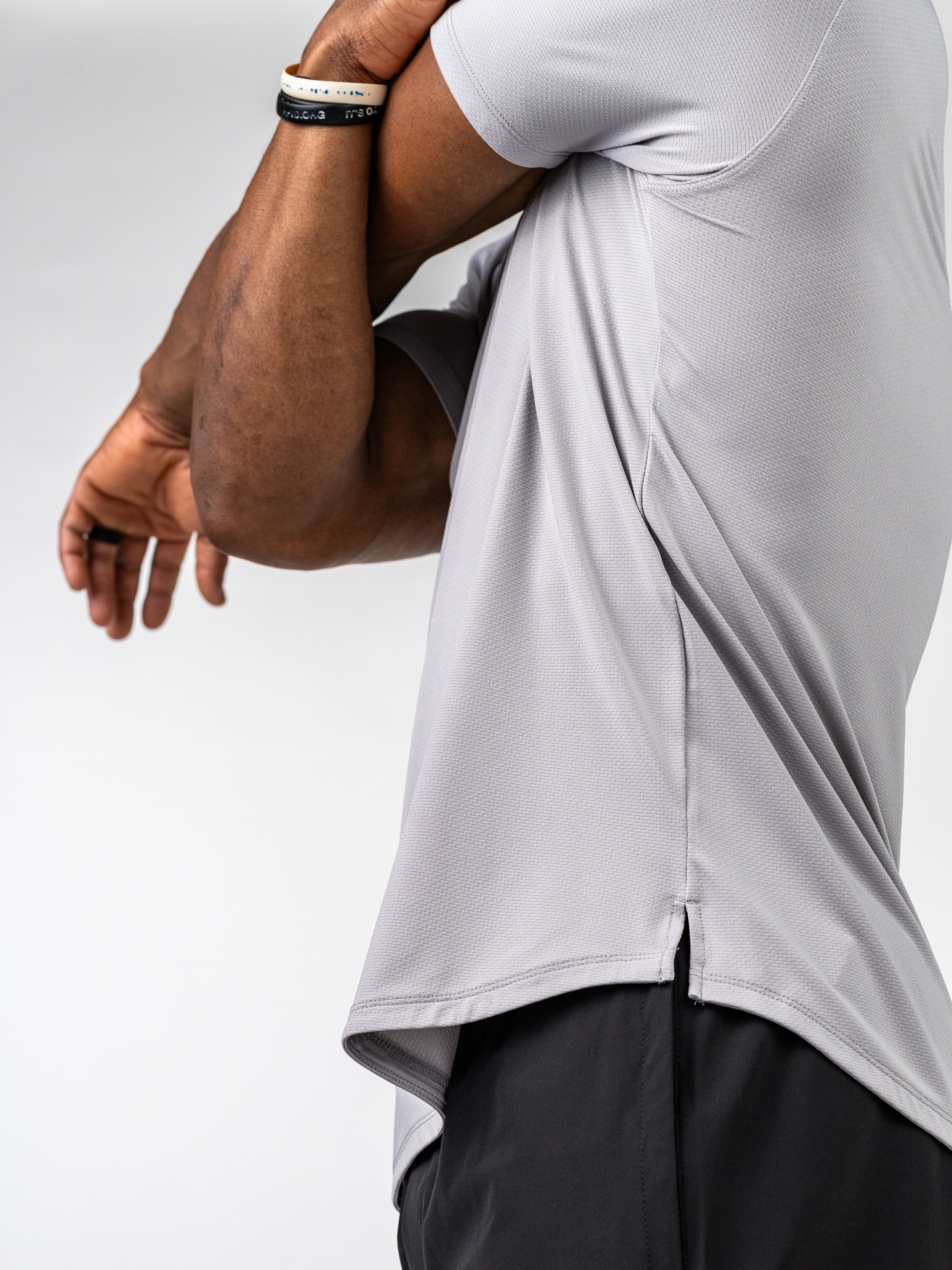 Athlete wearing a light grey Signature Tee made from breathable, stretch fabric designed for intense training and performance, shown mid-stretch against a neutral background.