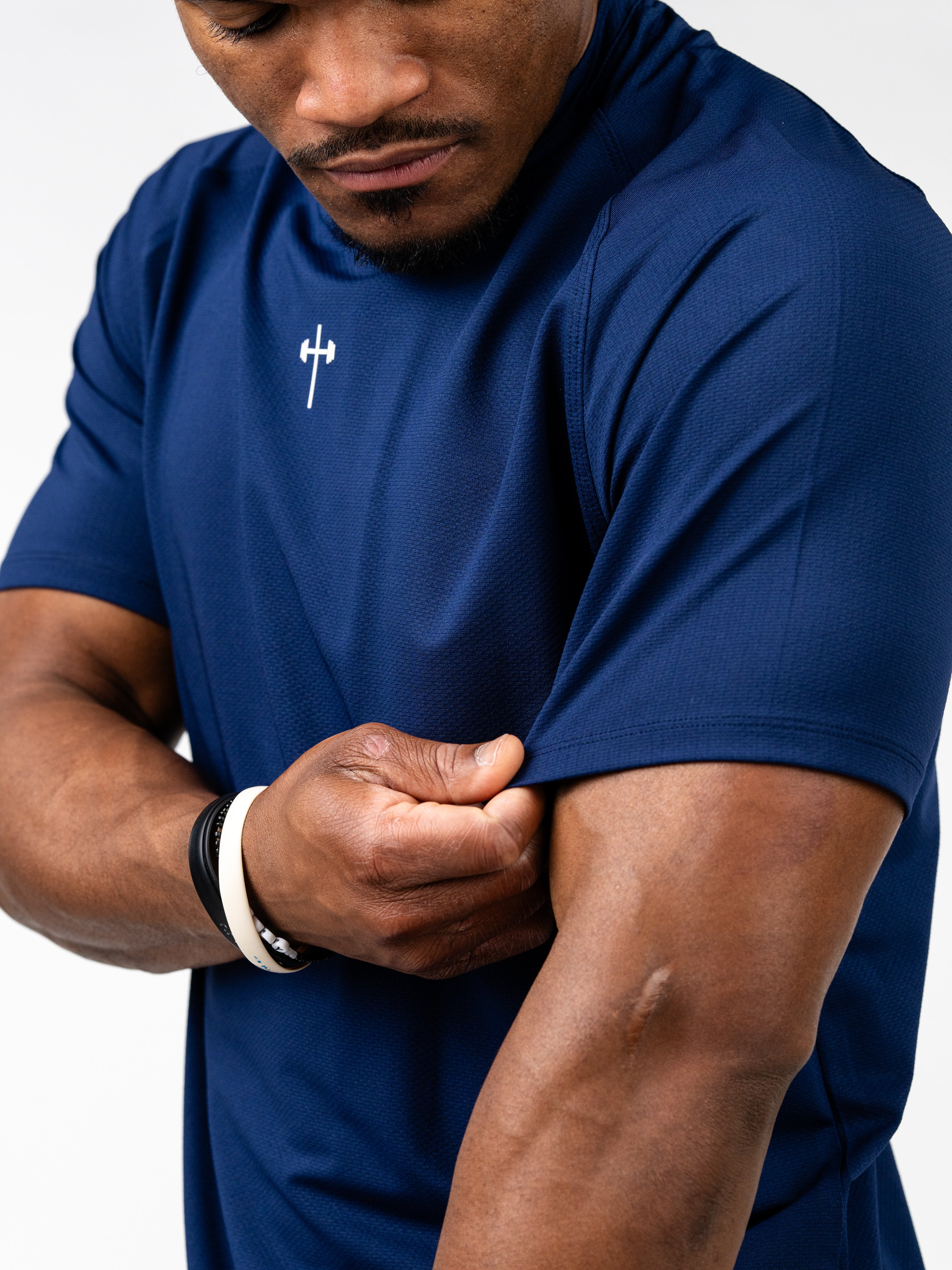 Man wearing a navy blue Signature Tee featuring a small white barbell cross logo on the chest, showcasing the breathable, stretch fabric designed for intense training and durability.
