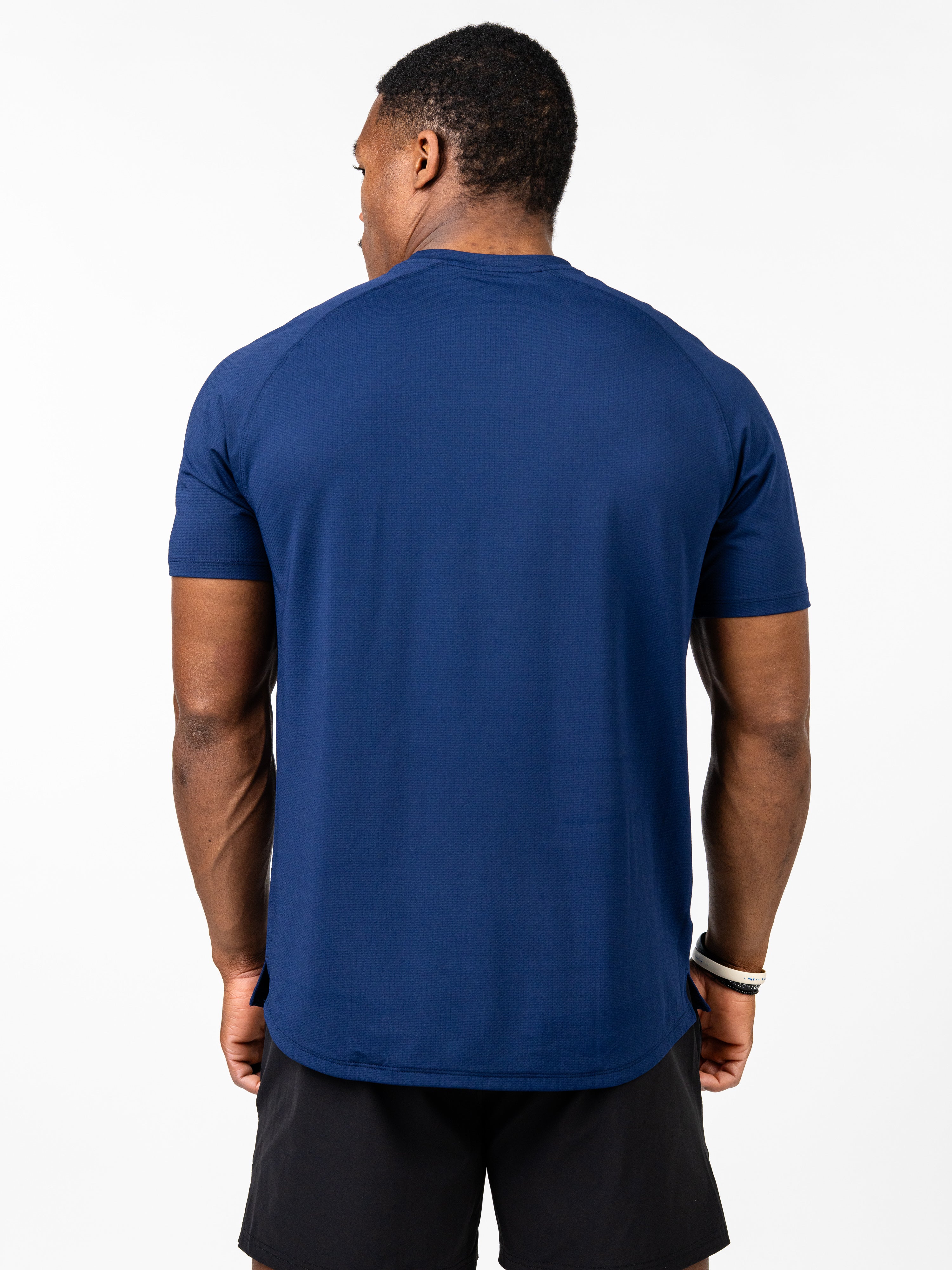 Man wearing a navy blue Signature Tee made from breathable, stretchy performance fabric, shown from the back, paired with black shorts in an athletic pose.