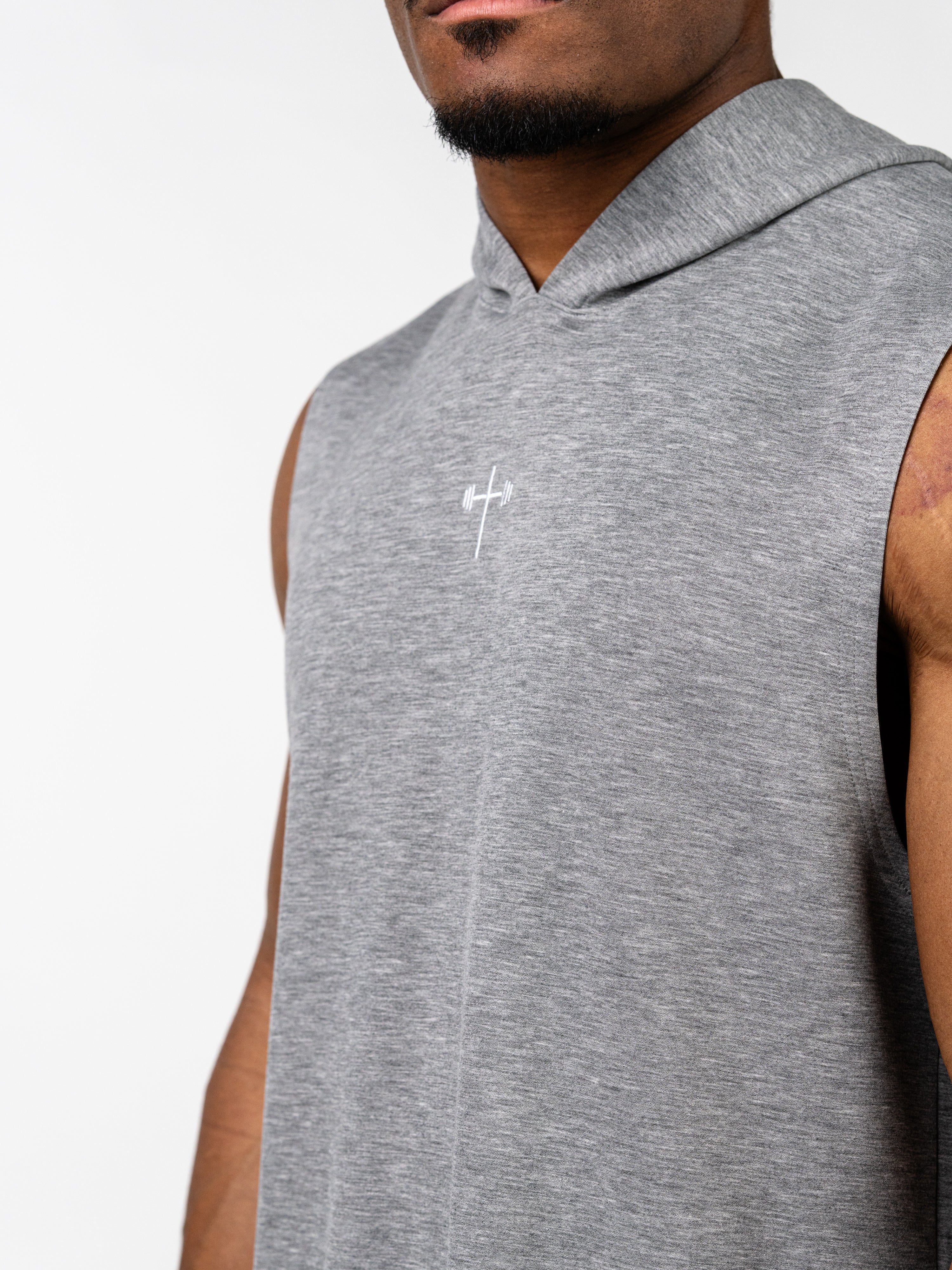 Close-up of a man wearing a gray Essential Sleeveless Hoodie with a subtle white Christian cross and barbell logo on the chest, designed for faith-based fitness and gym wear.