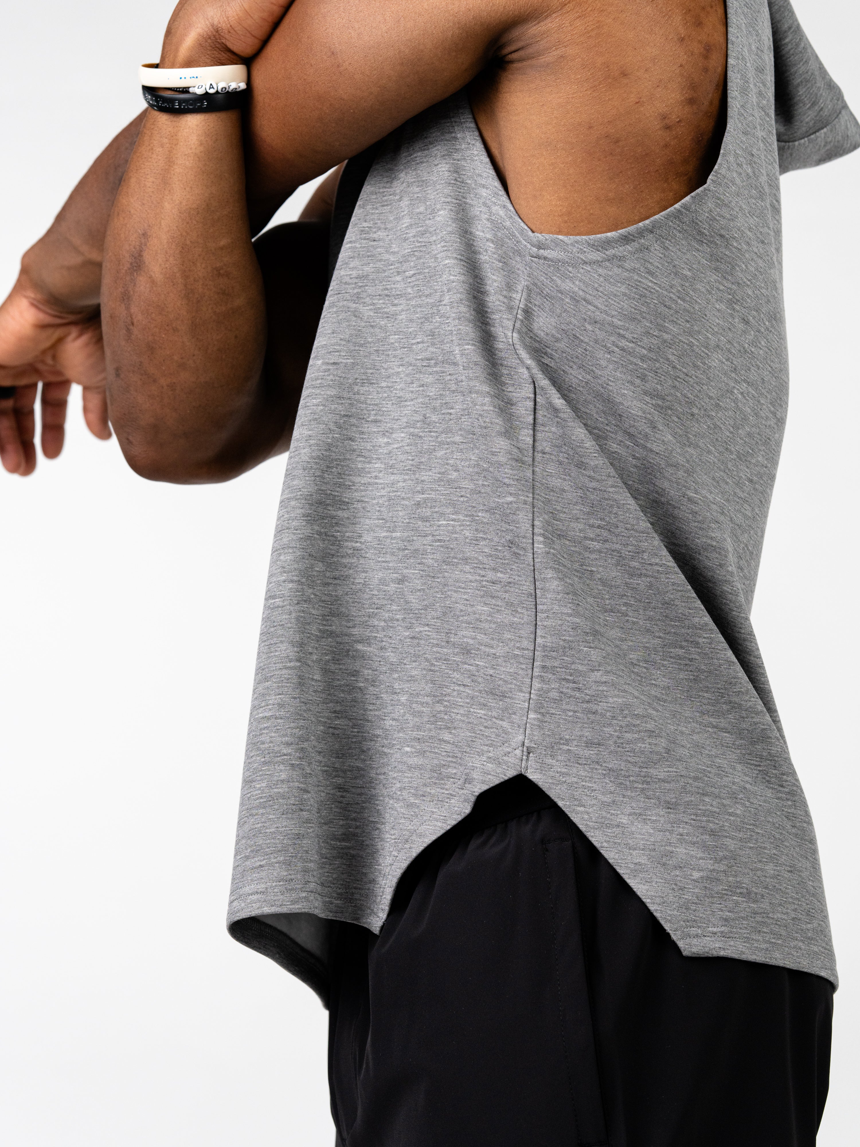 Close-up side view of a person wearing a gray Essential Sleeveless Hoodie, designed for unrestricted arm movement, paired with black workout shorts, highlighting lightweight fabric and athletic fit.