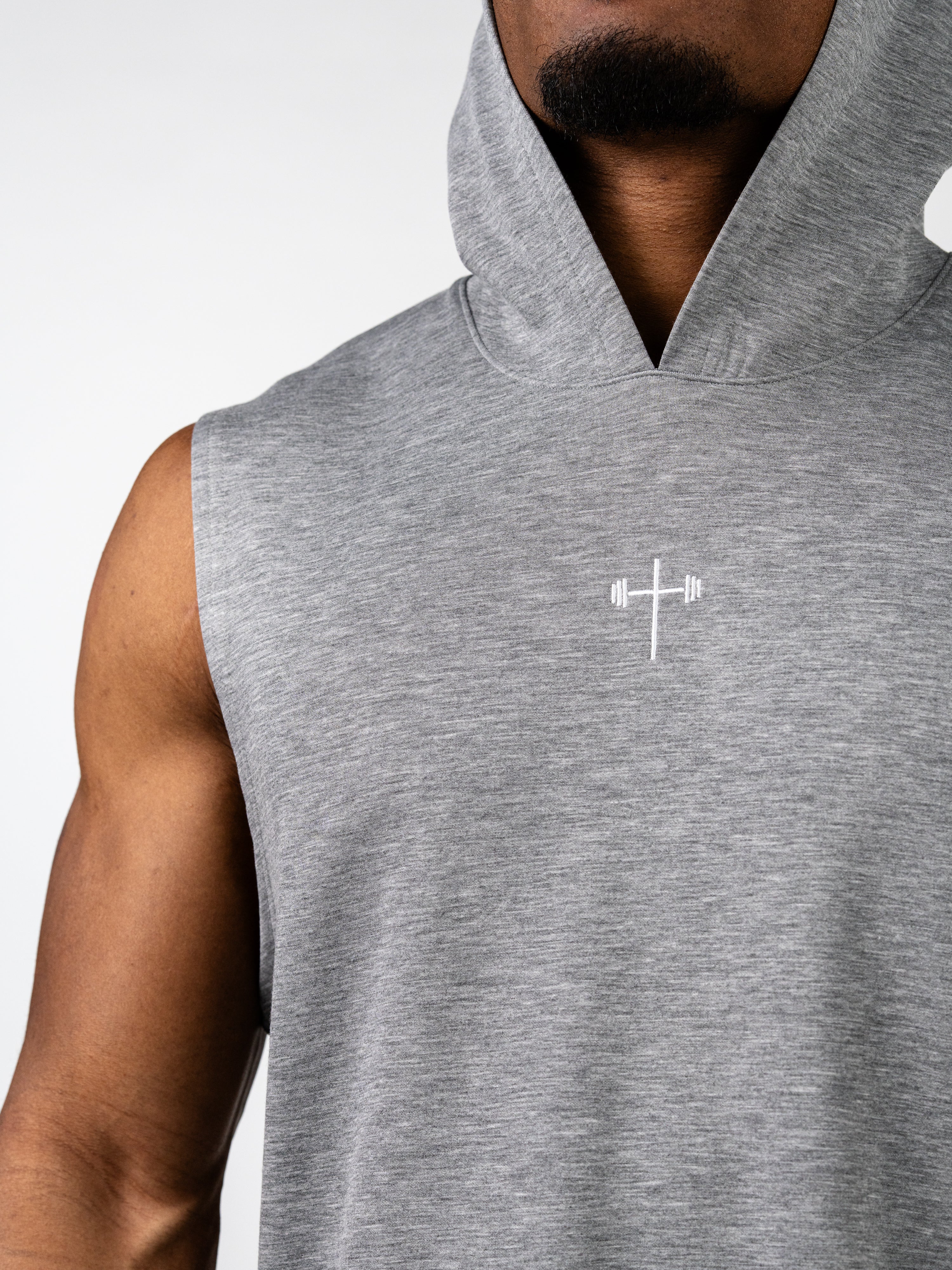 Close-up of a man wearing a gray Essential Sleeveless Hoodie featuring a subtle white Christian cross with barbell embroidery on the chest, designed for athletic training and comfort.