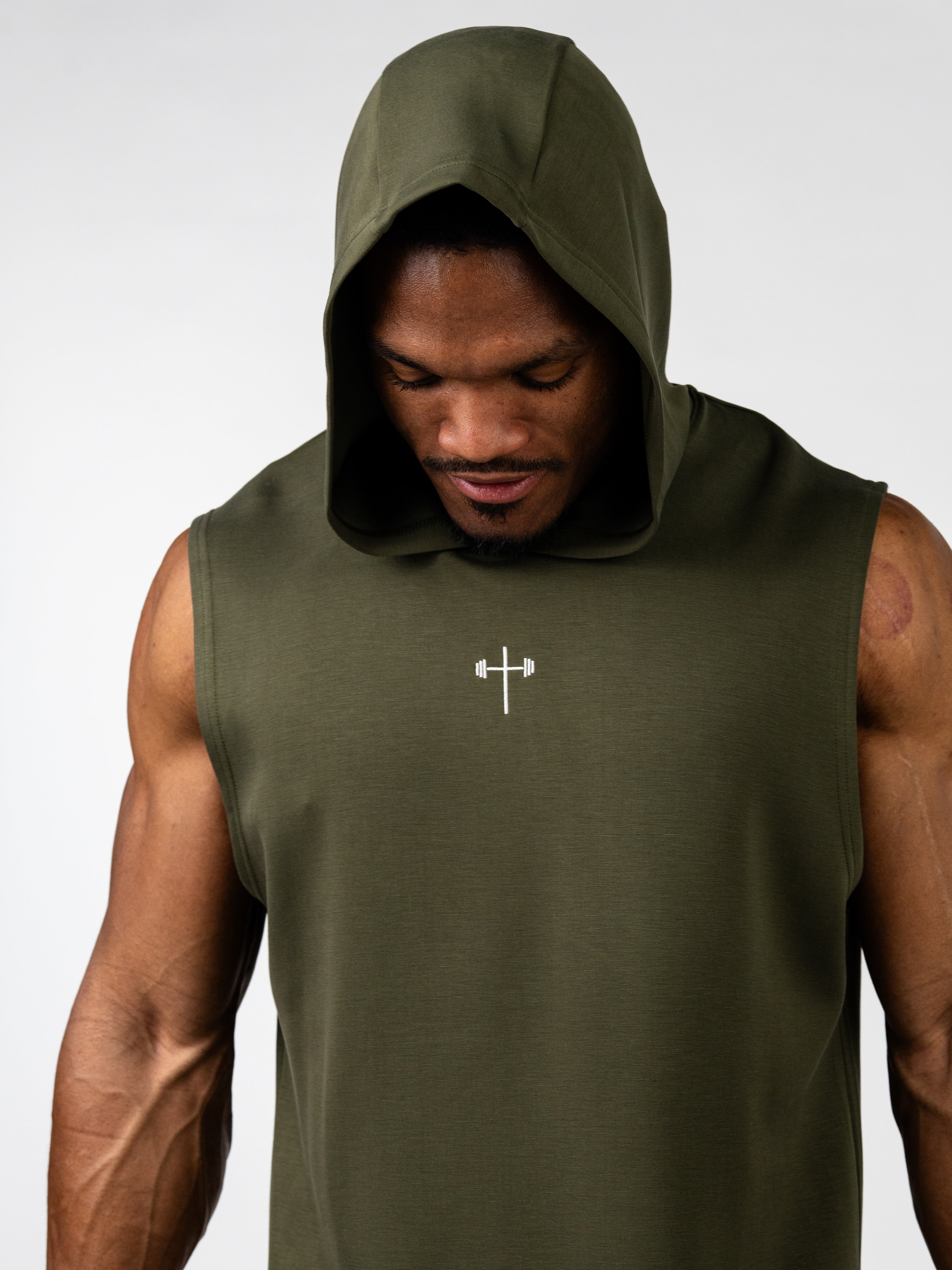 Athletic man wearing an olive green Essential Sleeveless Hoodie with a hood up, featuring a small white cross and barbell symbol on the chest, representing Christian fitness apparel.
