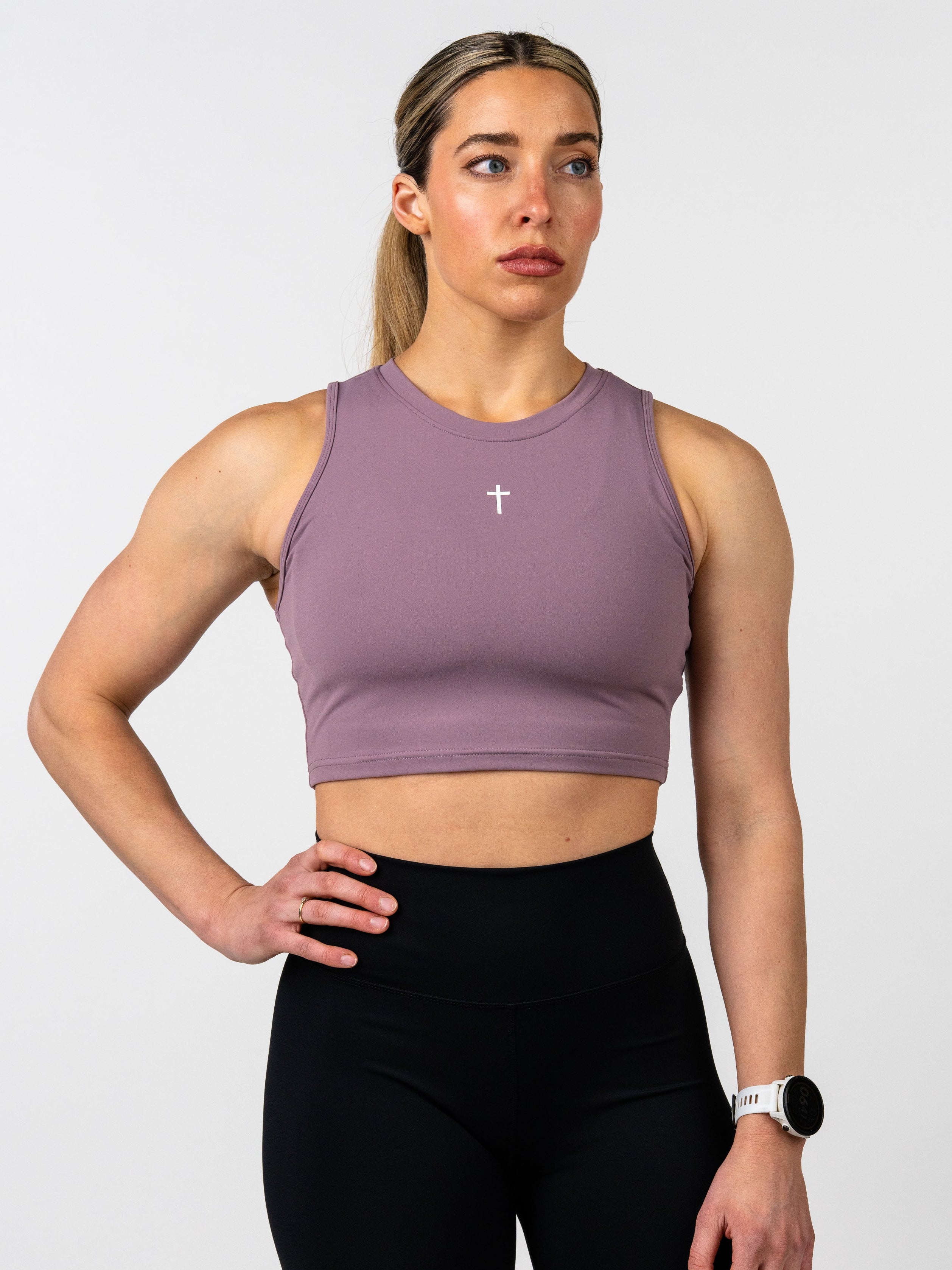 Woman wearing a mauve sports bra and black leggings on a white background