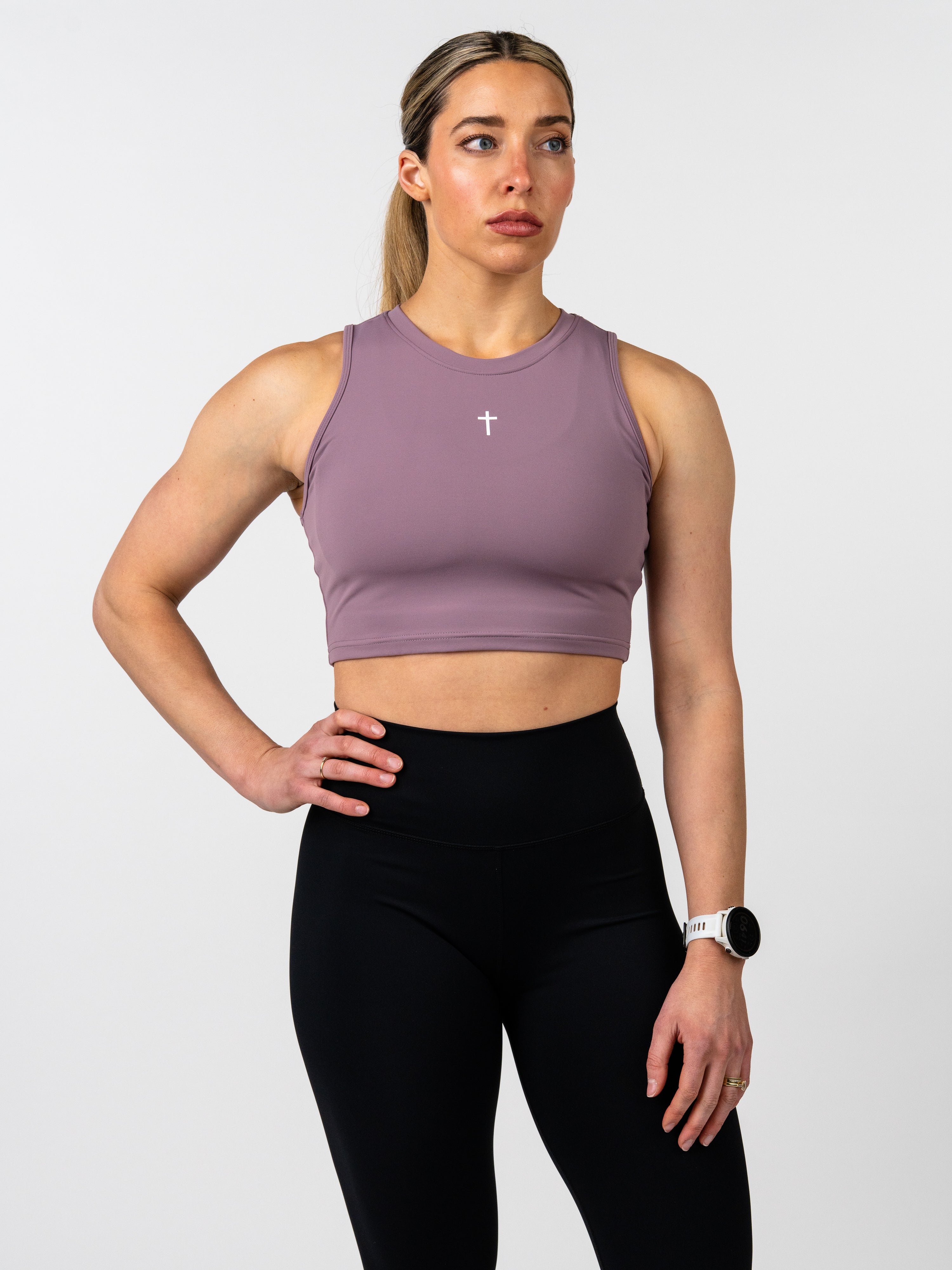 Woman wearing a mauve sports bra and black leggings on a white background