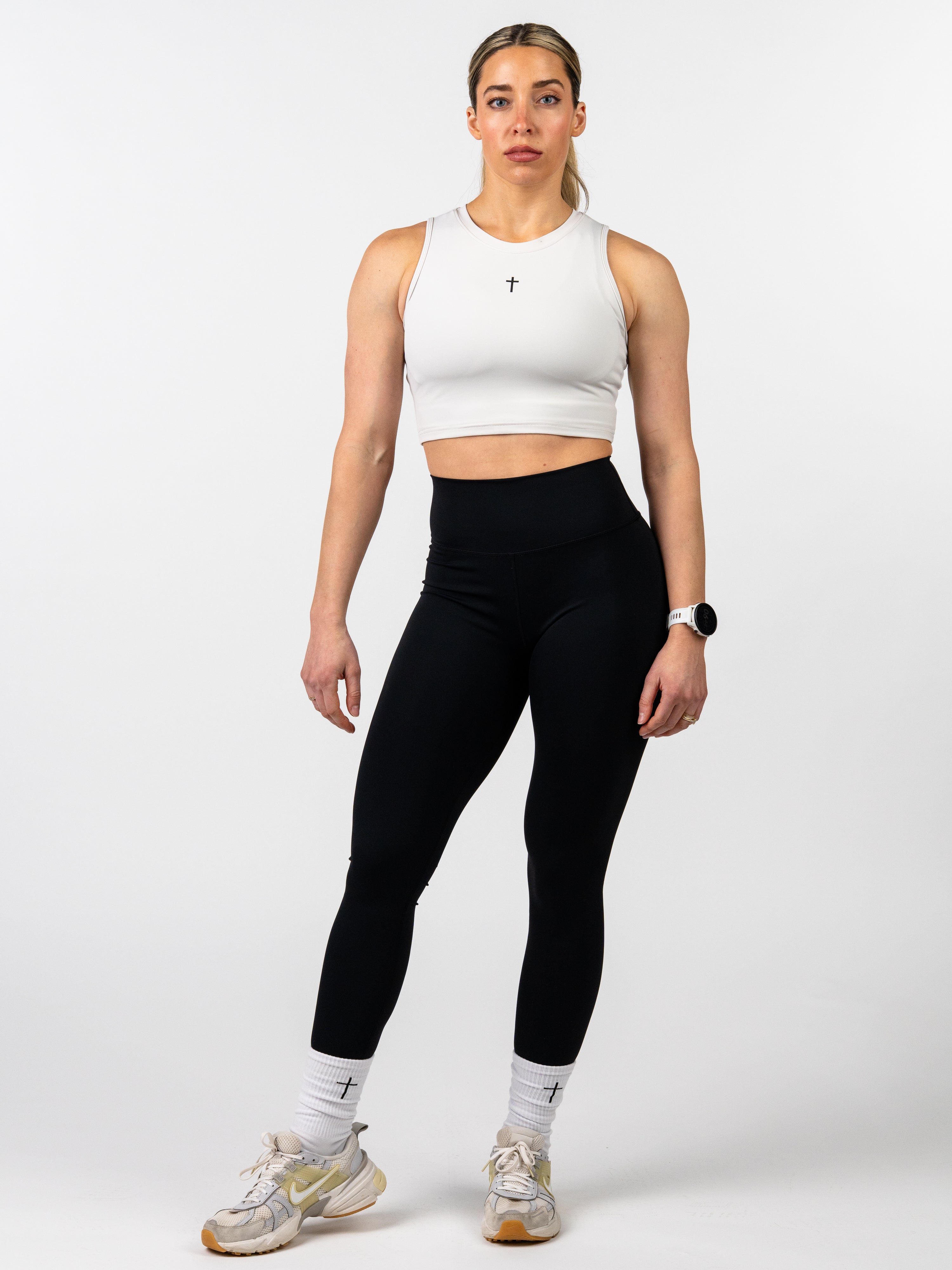 Woman wearing a white tank top and black leggings on a white background