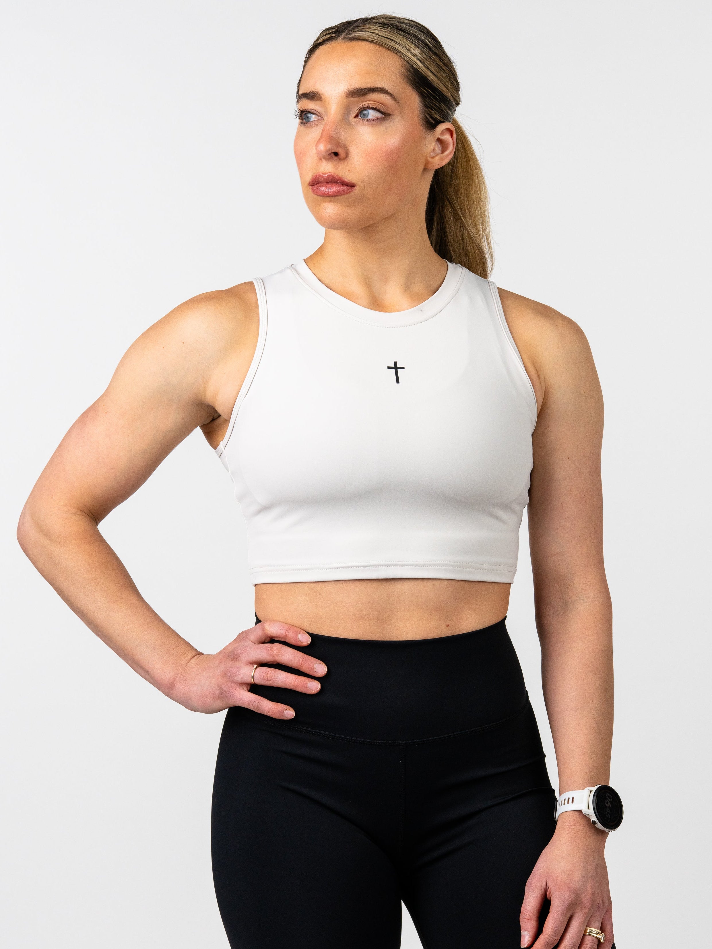 Woman wearing a white crop top and black leggings on a light gray background