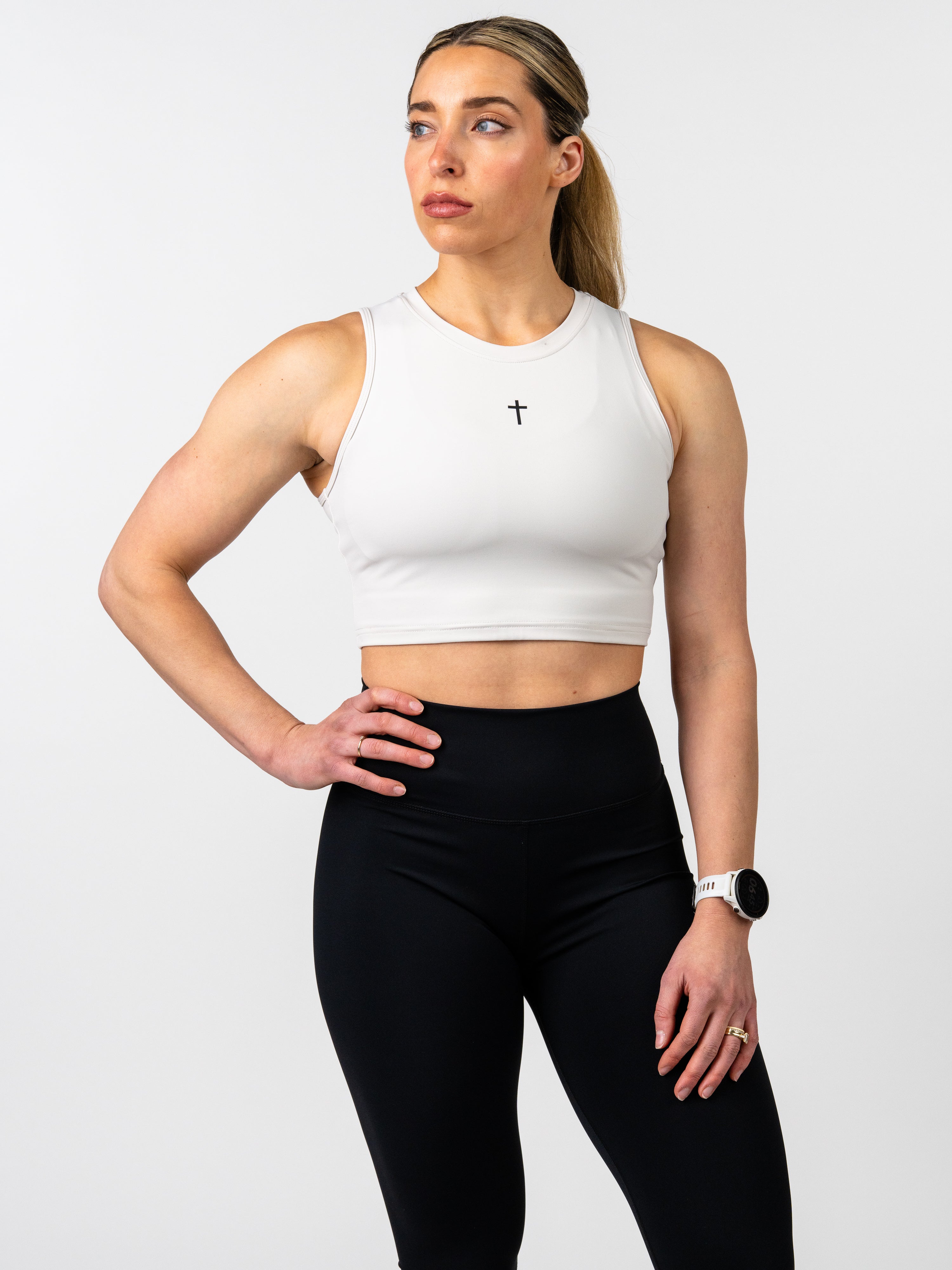 Woman wearing a white crop top and black leggings on a light gray background