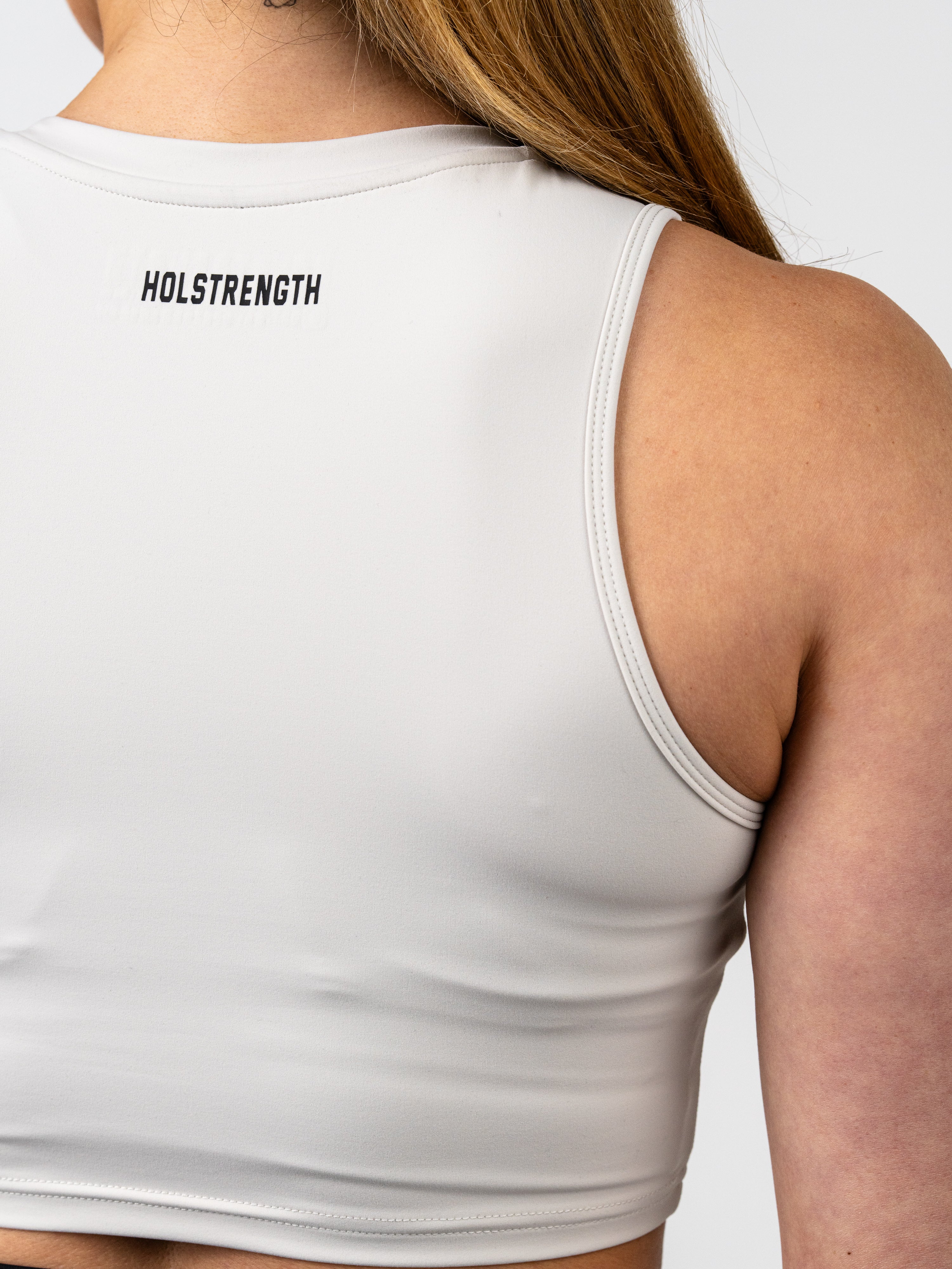 Close-up view of a woman wearing a light-colored Vital Cross Combat Top, showing the smooth fabric and HolStrength logo printed at the upper back of the fitted athletic tank.