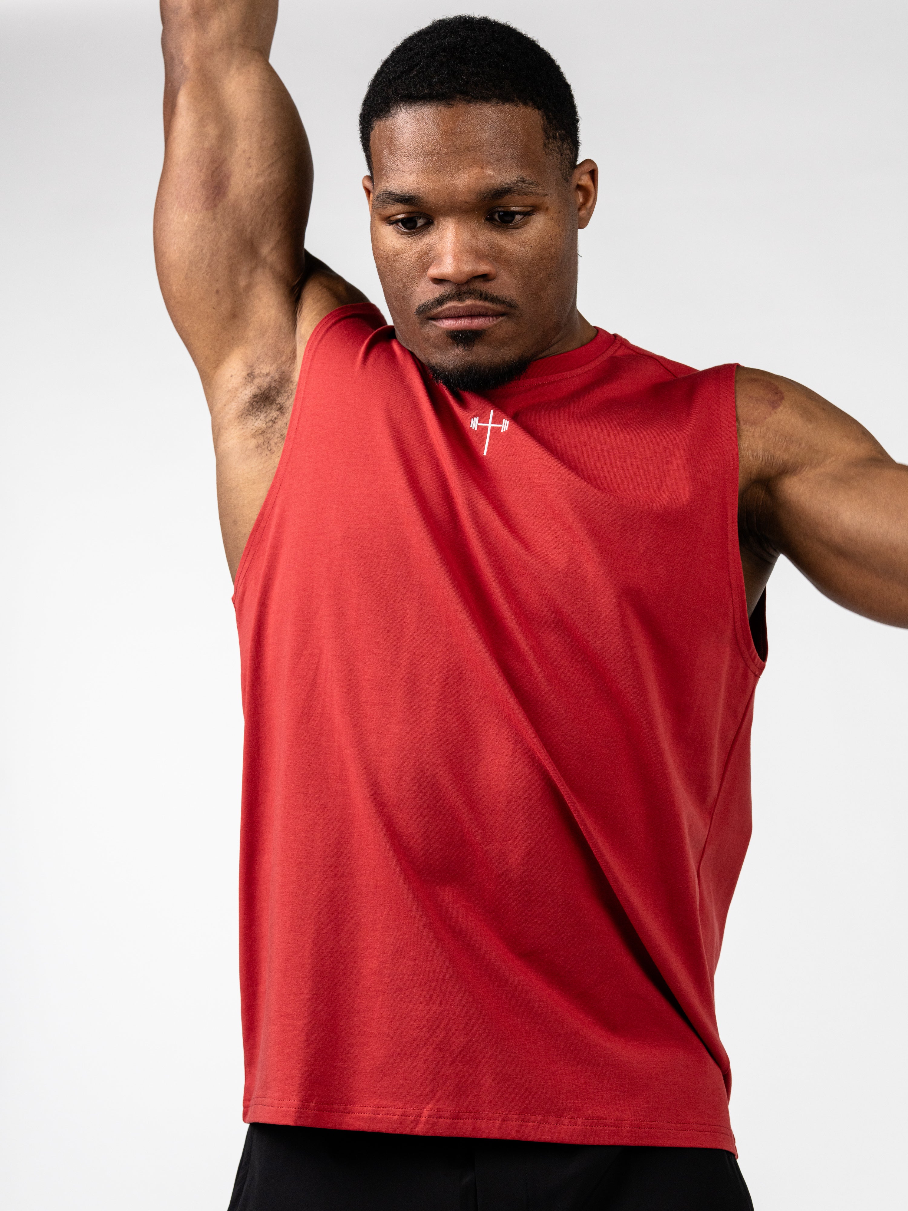 Man wearing a red Vital Cross Sleeveless Tank lifting his arm, featuring a subtle Christian cross and barbell design, ideal for faith-based fitness and activewear.