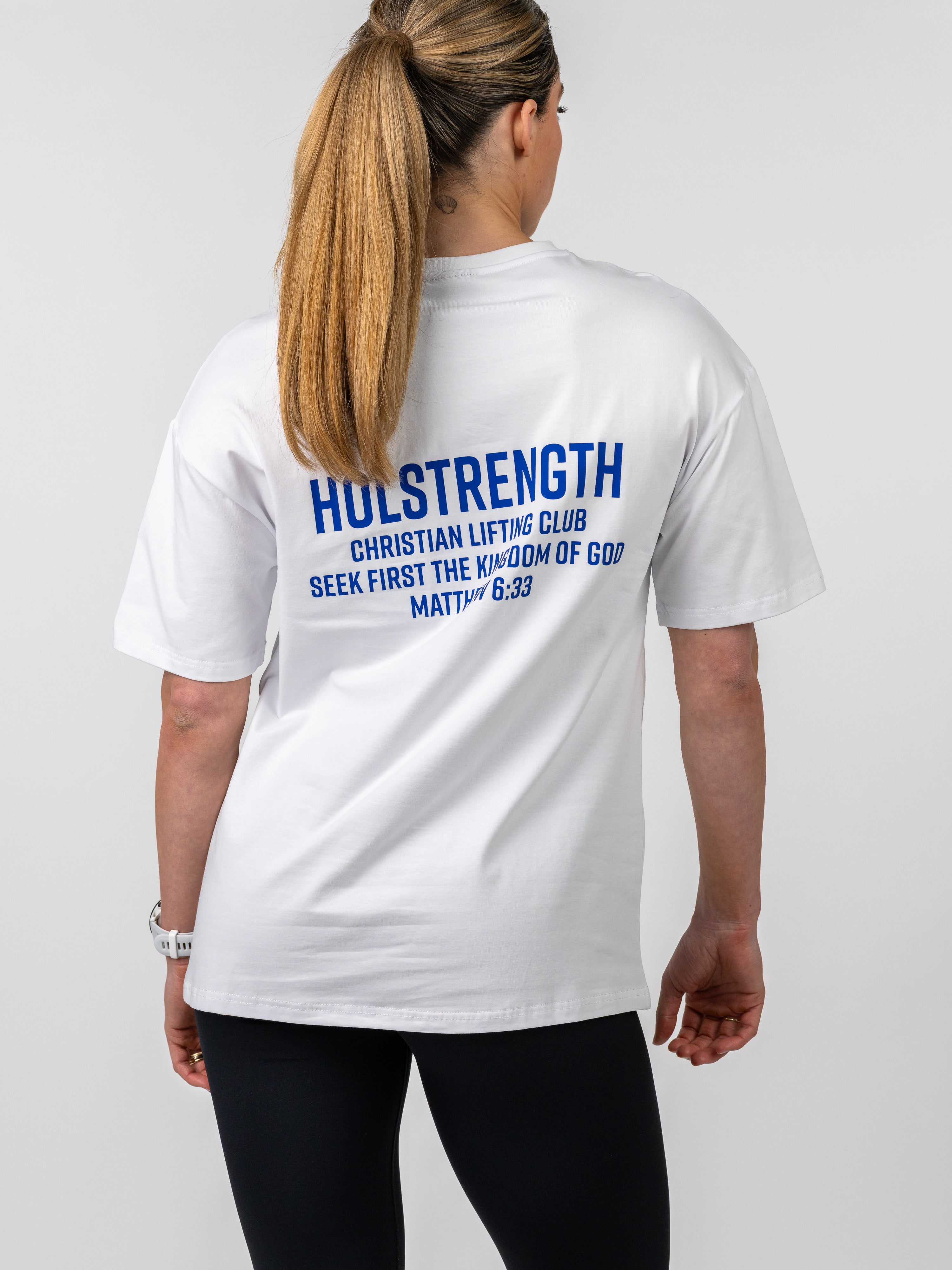 Woman seen from behind wearing a white Women's Lifting Club Oversized Tee with blue text referencing Christian lifting club and a Bible verse, paired with black leggings.