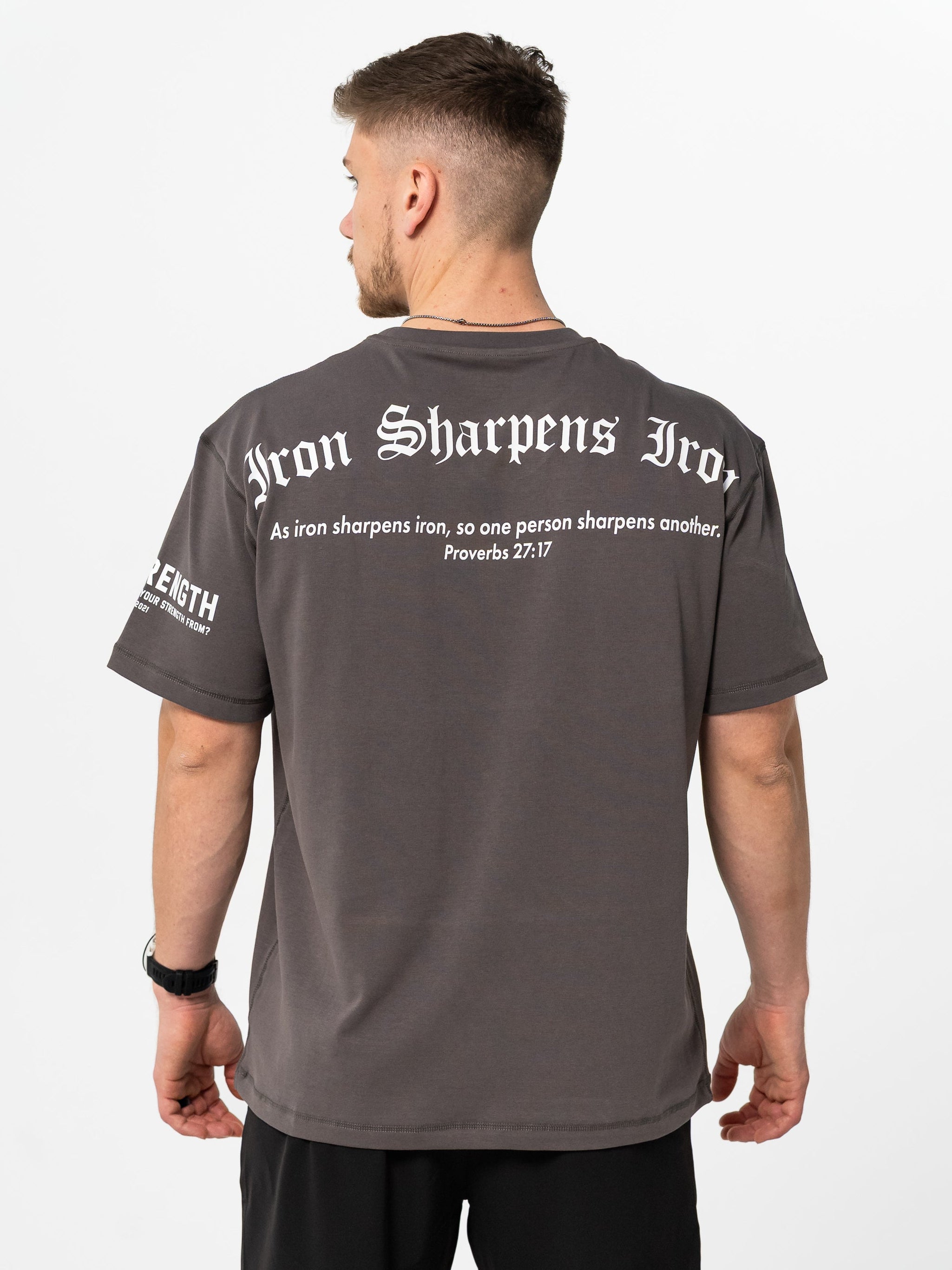 Man wearing a iron gray t-shirt with text on the back, standing against a white background
