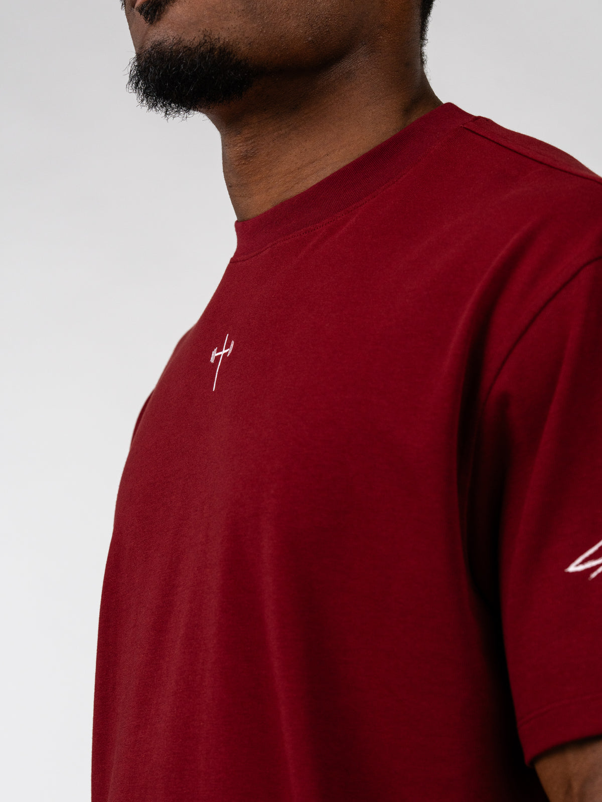 Sacred Heart Premium Oversized Tee in deep red with a relaxed fit, subtle white cross chest detail, and matching sleeve graphic modeled as Christian apparel
