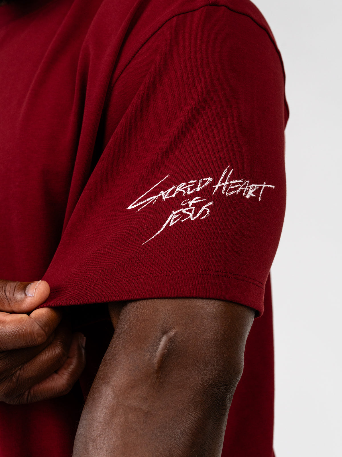 Sacred Heart Premium Oversized Tee in burgundy with a white Sacred Heart sleeve graphic shown in close up detail as Christian apparel