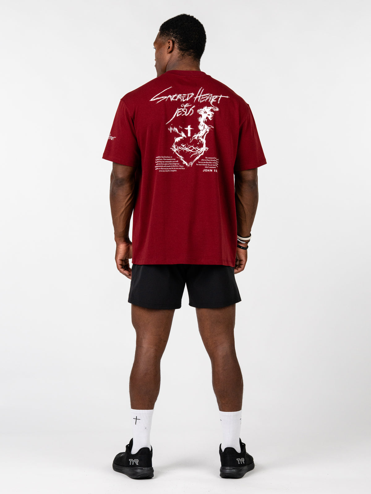 Sacred Heart Premium Oversized Tee shown from the back in red with white sacred heart artwork styled with black shorts for Christian apparel lovers