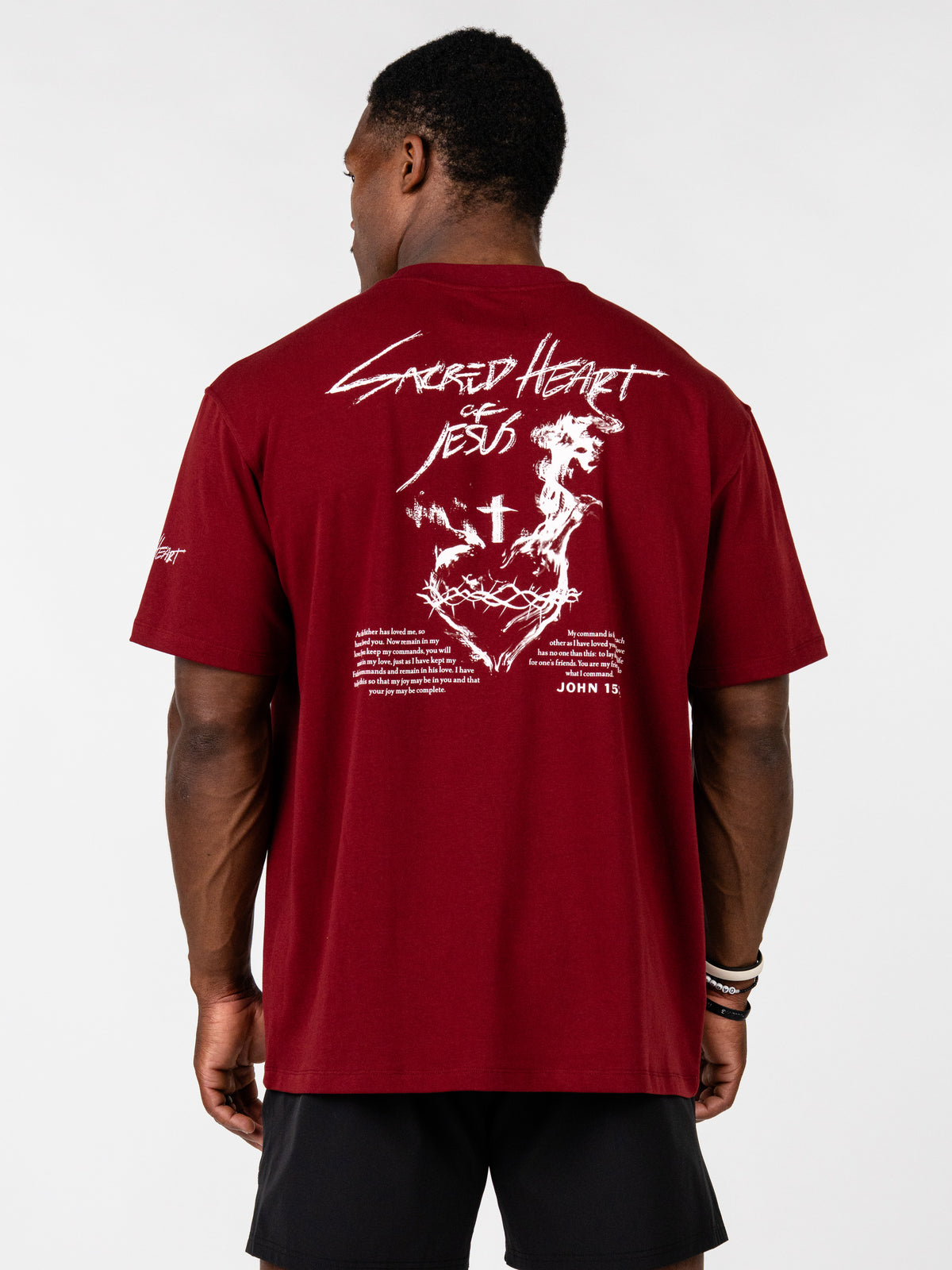Sacred Heart Premium Oversized Tee in burgundy with bold Sacred Heart cross artwork and John 15 scripture graphic shown on the back with black shorts